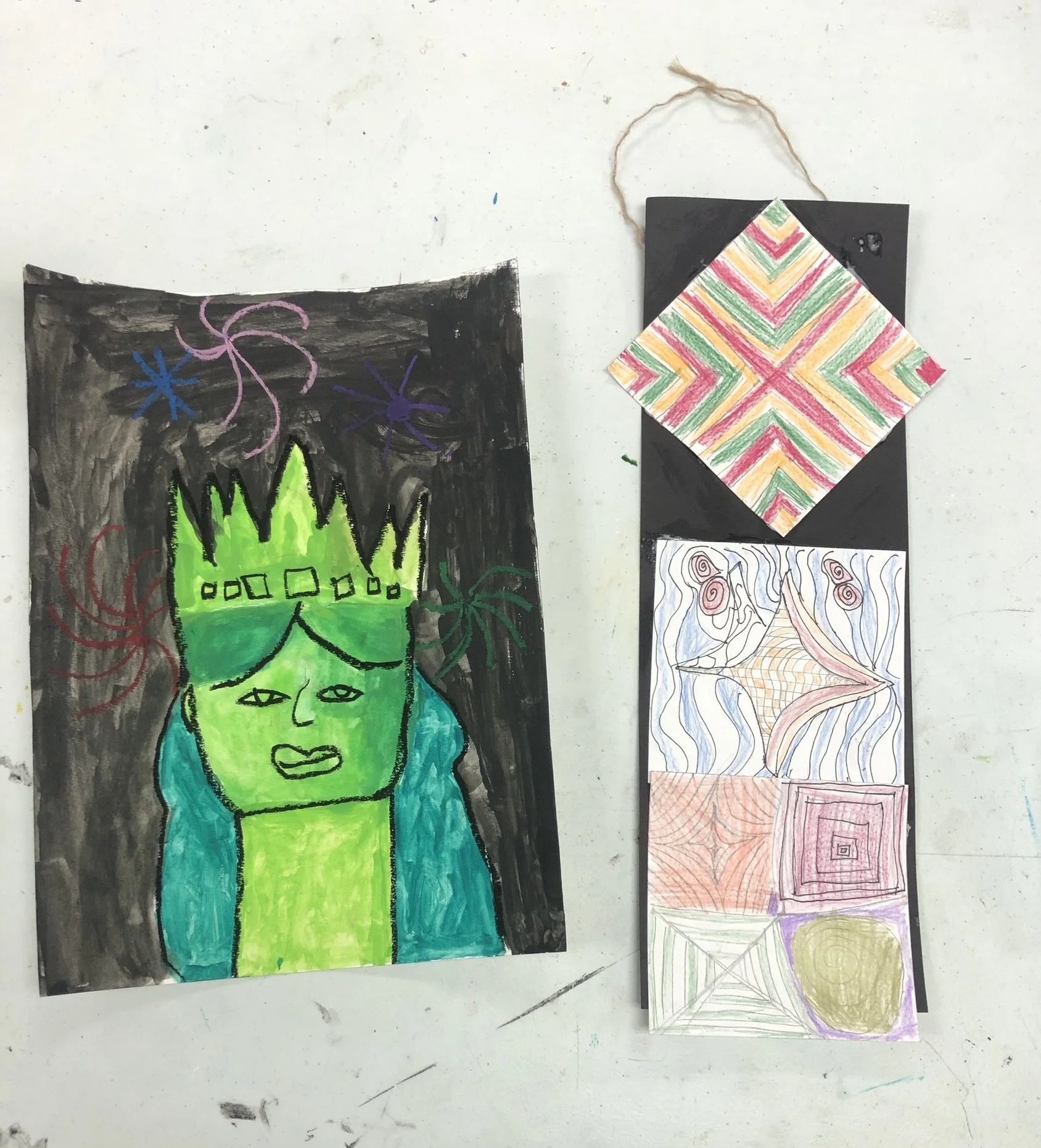 Colorful drawings including a green face with a crown and long blue hair, surrounded by firework-like designs, with additional abstract watercolor and colored pencil patterns on smaller paper.