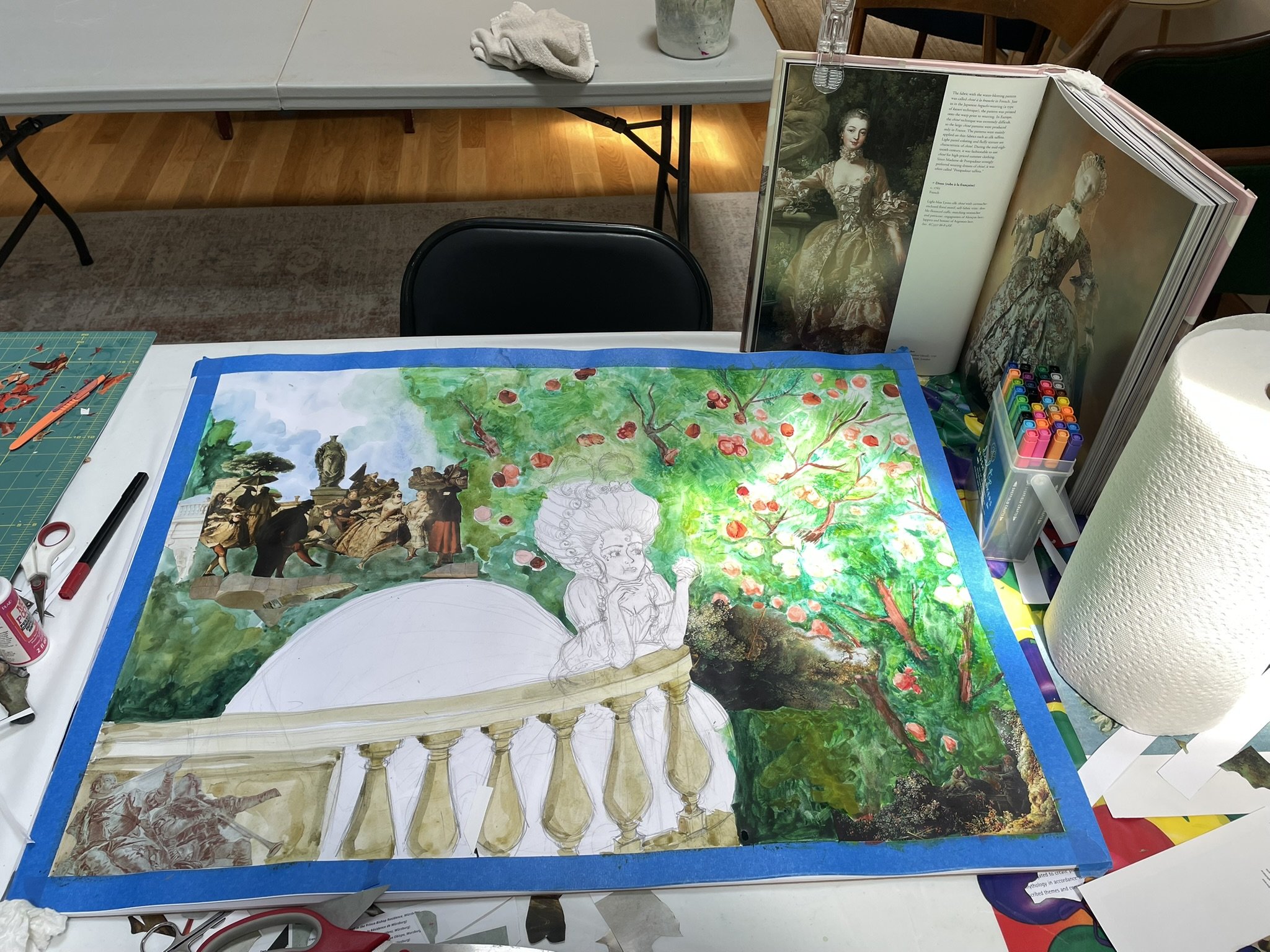 A watercolor painting in progress on a desk, featuring a statue on a fountain, a woman with an elaborate hairstyle, and a lush green and pink flowering tree. Art supplies and reference books are nearby.