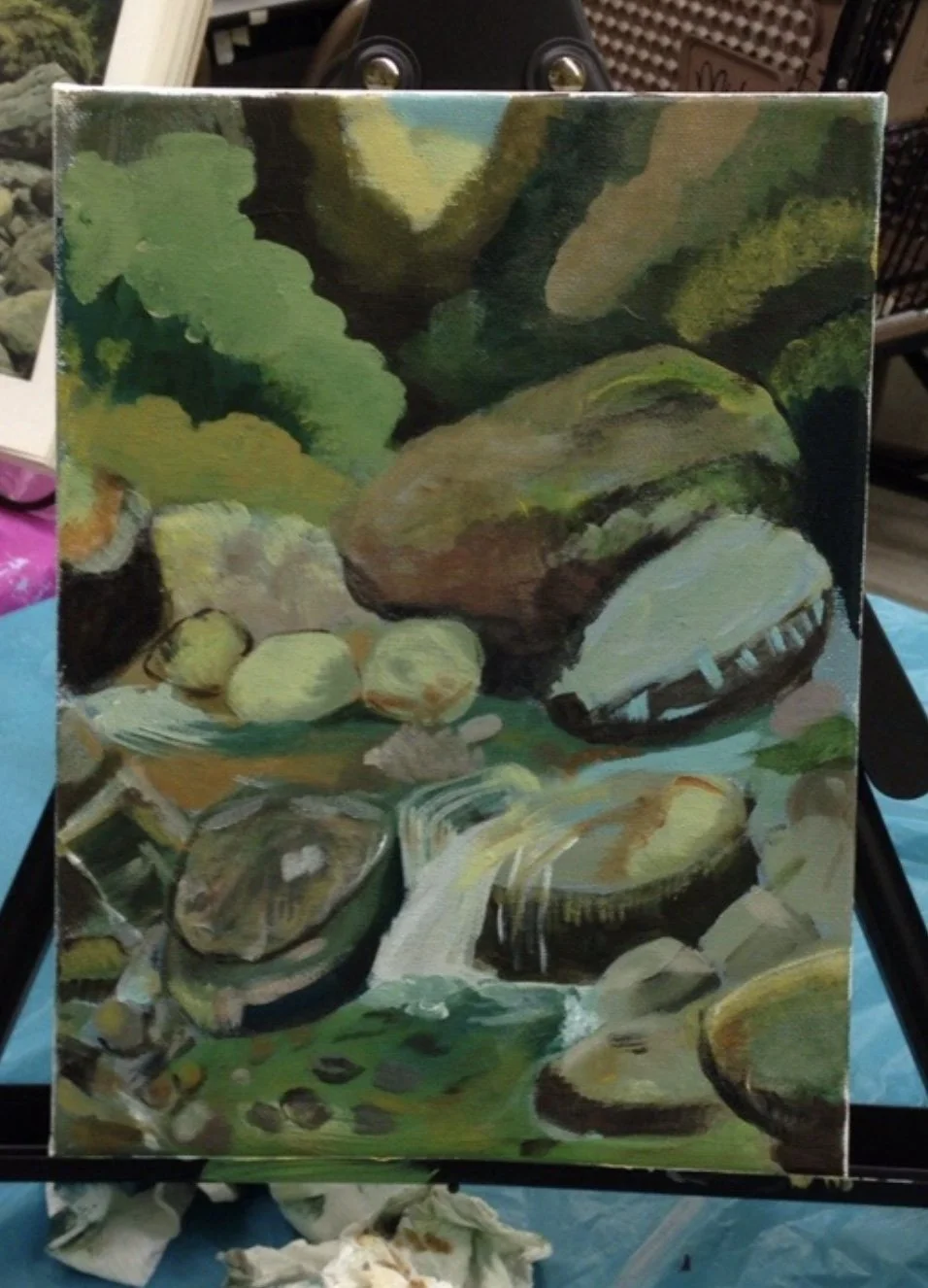 A small painting of a creek with rocks and green foliage. The painting depicts a waterfall or flowing water among large rocks and plants.