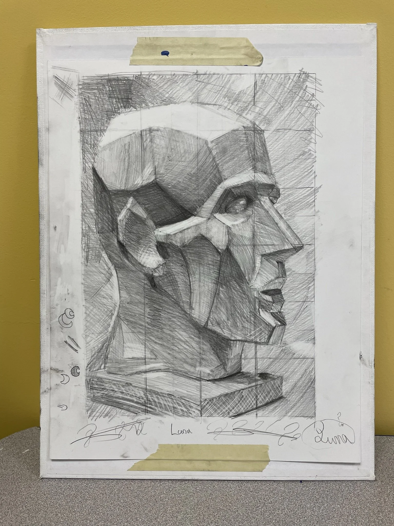 A detailed pencil sketch of a geometric bust sculpture of a human head in profile view. The drawing shows multiple intersecting planes and facets, emphasizing a cubist style. The sketch includes shading and grid lines and is taped to a wall with mask