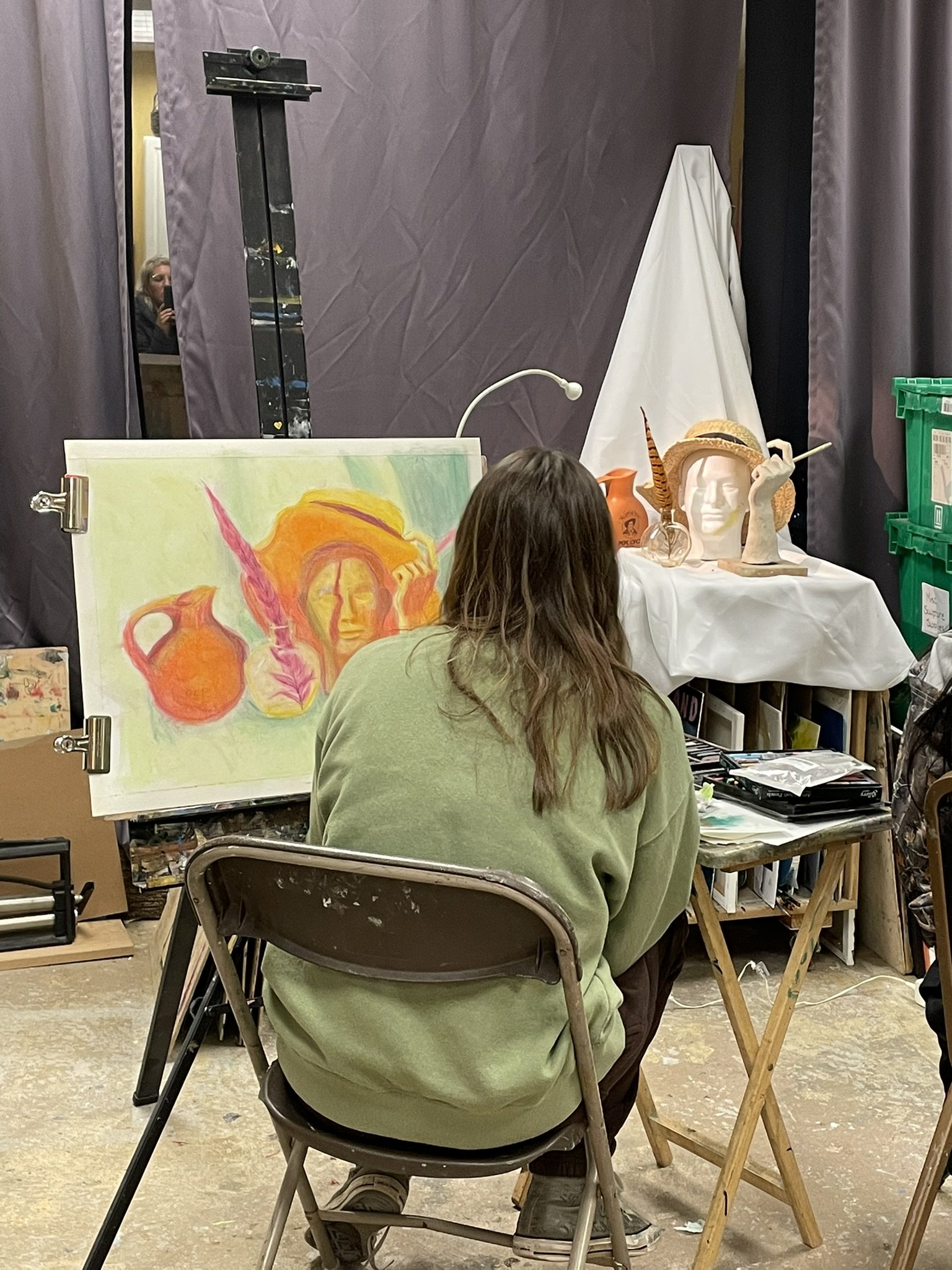 Artist painting a colorful portrait of a woman with long hair and a hat, with two orange vases in the background.