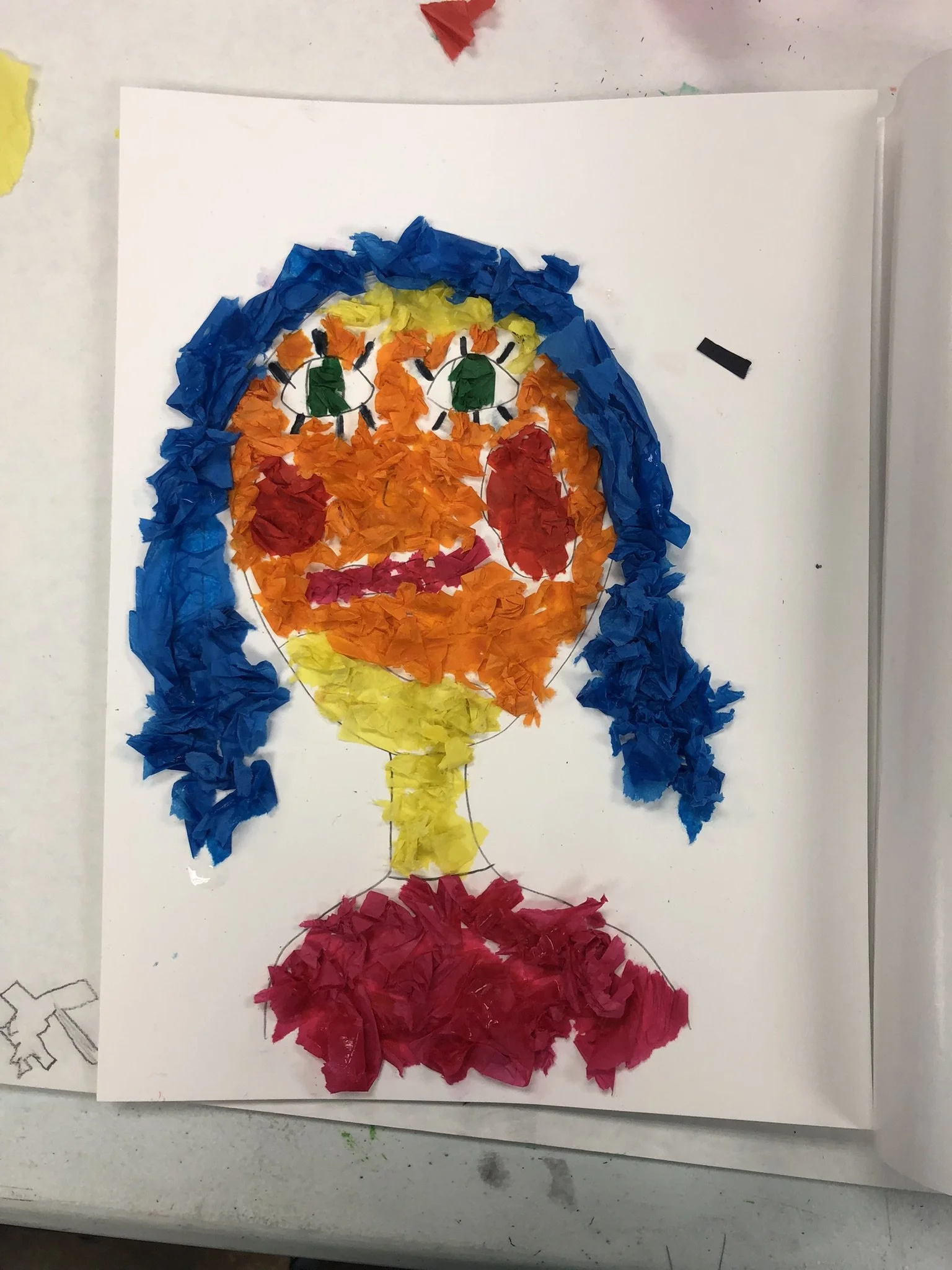 A colorful collage of a face made with torn pieces of paper, featuring blue hair, green eyes, red cheeks, yellow neck, and red clothing, assembled on a white background.