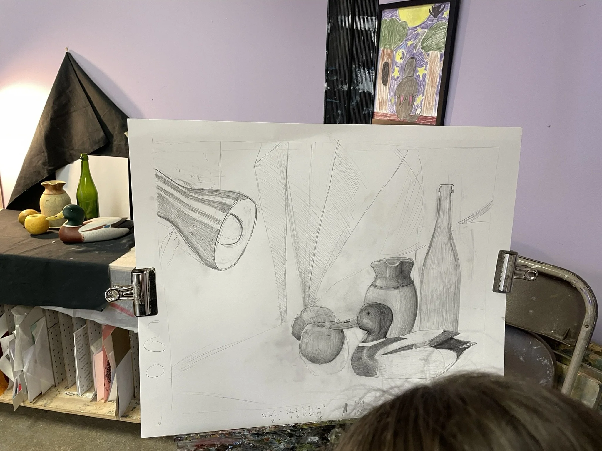 A large sheet of paper with a pencil sketch of a still life with vases, a duck figurine, and fruits, leaning on clip clips, in an art studio.