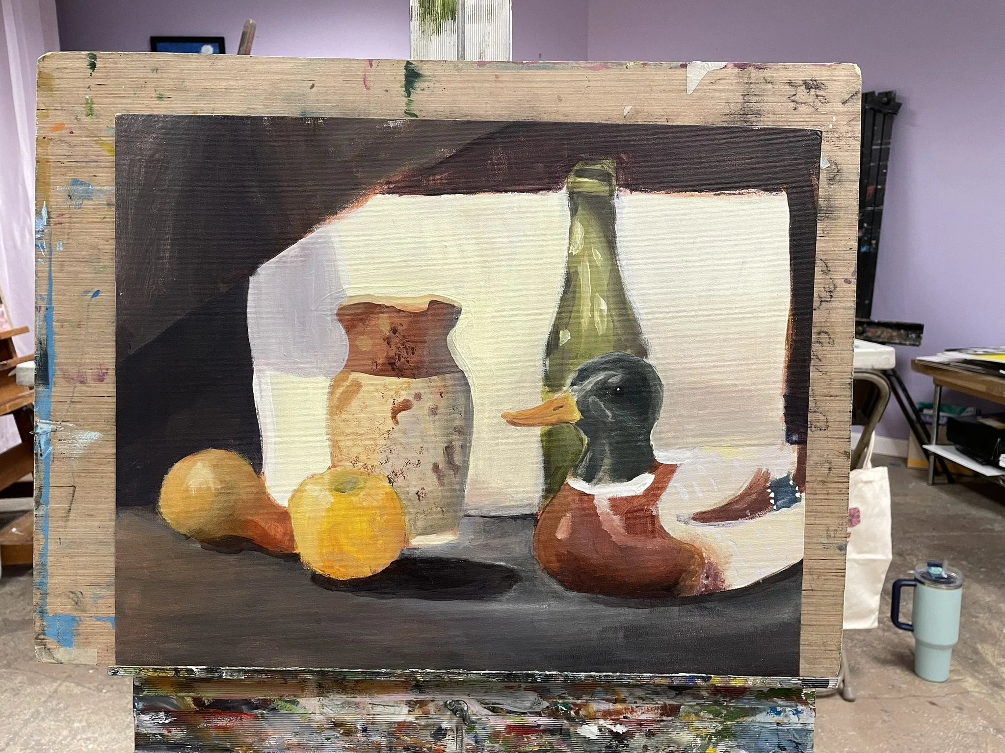 A still life painting on an easel featuring two apples, a ceramic vase, a green bottle, and a ceramic duck figurine, with a purple wall and frame in the background.