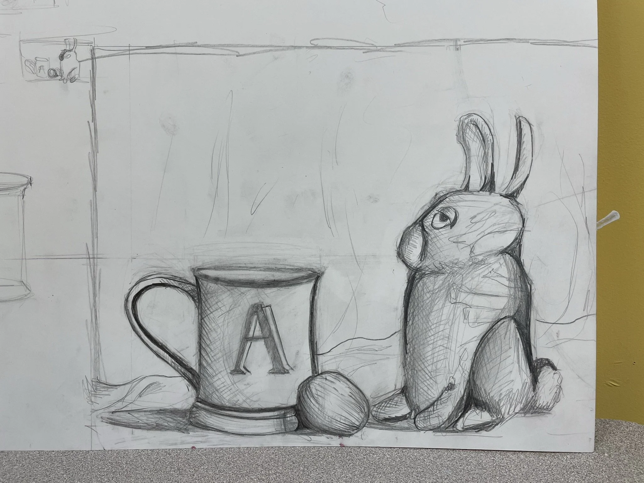 Sketch of a still life scene with a coffee mug labeled with an 'A', a walnut, and a rabbit drawing on paper, placed on a surface against a wall.