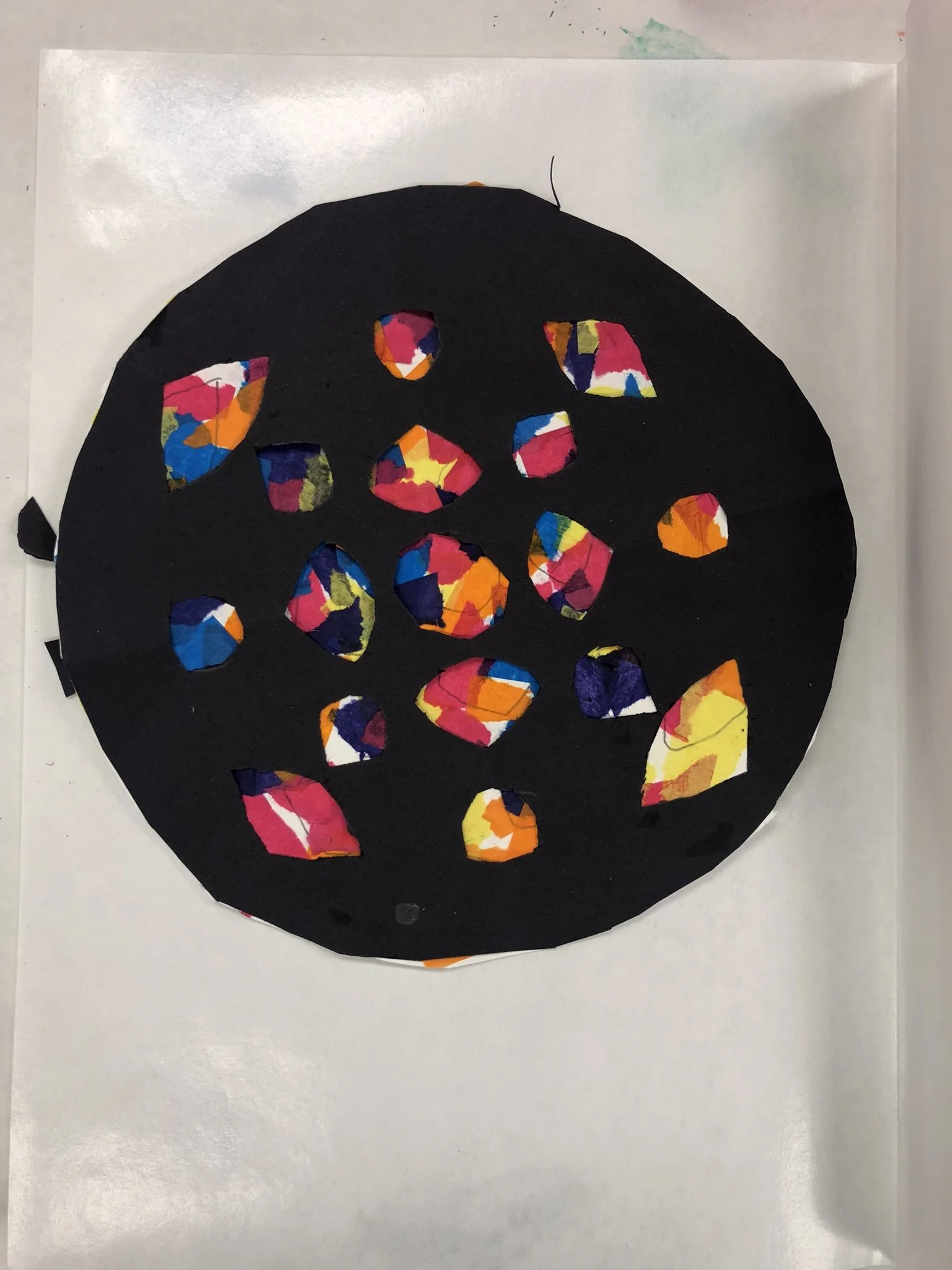 Decorative black circle with colorful torn paper pieces resembling a Halloween-themed picture, possibly a face or pumpkin.