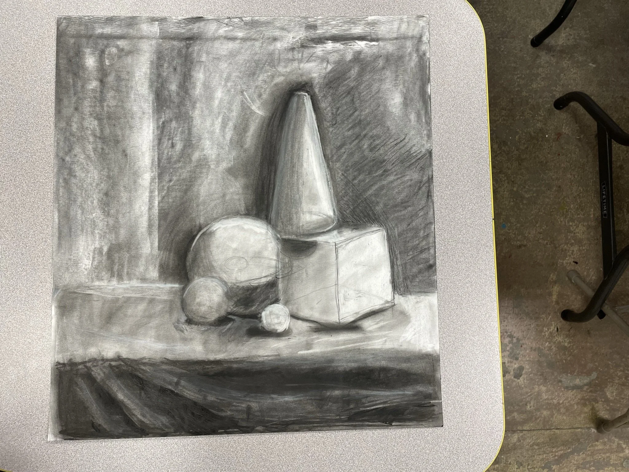 A grayscale still life sketch of geometric objects, including spheres, a cone, and a cube, arranged on a table with a textured background.