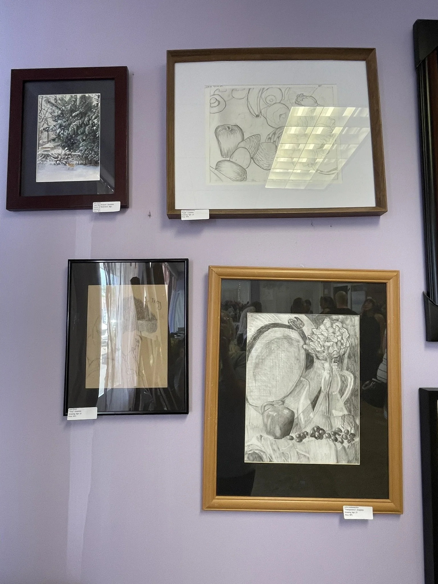 Four framed artworks on a purple wall, including a black and white landscape, a pencil drawing of vegetables, a sketch of a still life with a kettle, vase, and berries, and another art piece partially visible on the right.
