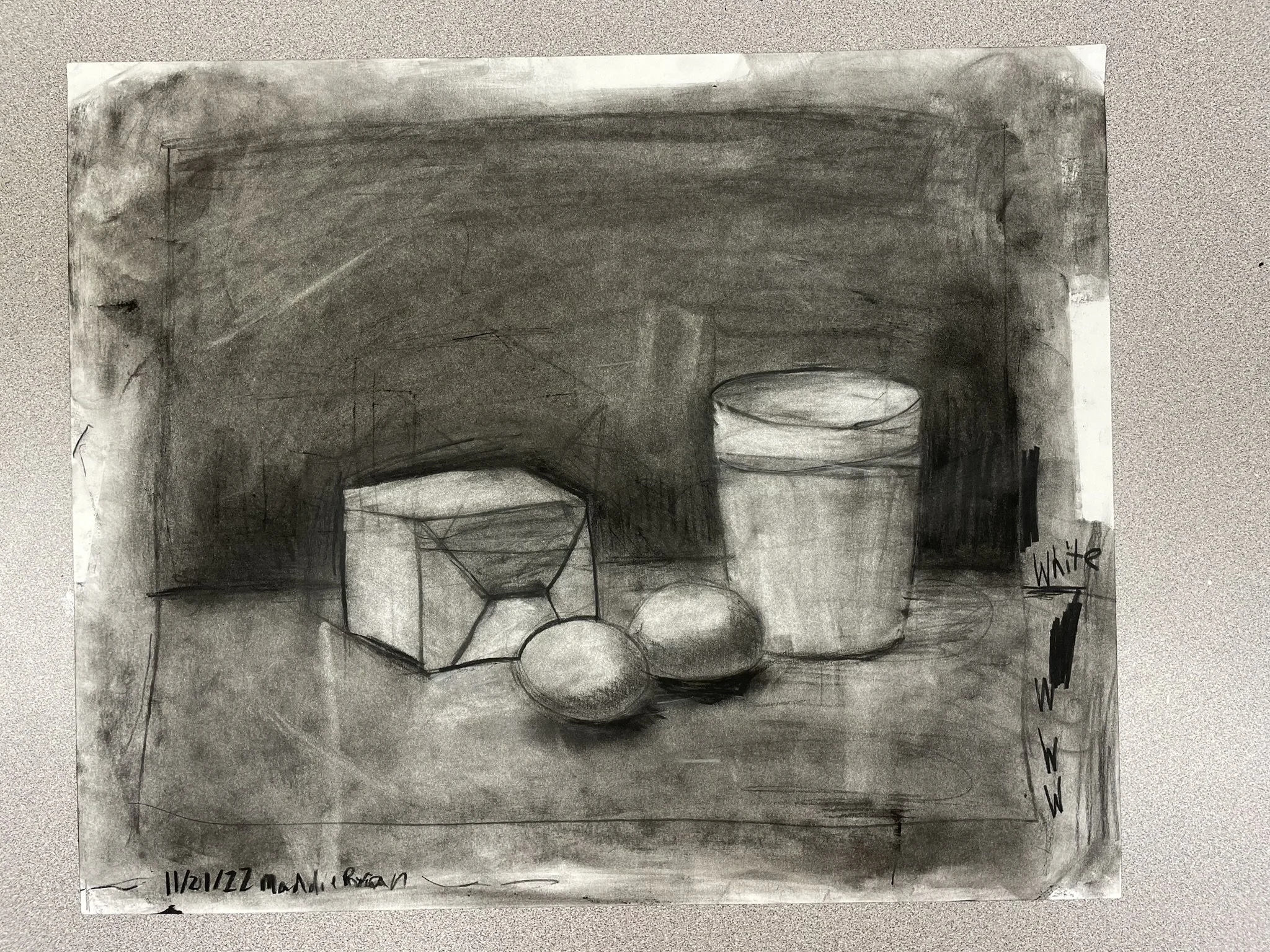 A black and white still life sketch featuring a cube, two round objects, a tall cylindrical jar with a band near the top, and a small rectangular block on a wooden surface. The background is shaded dark, with some light areas, and the objects are sha