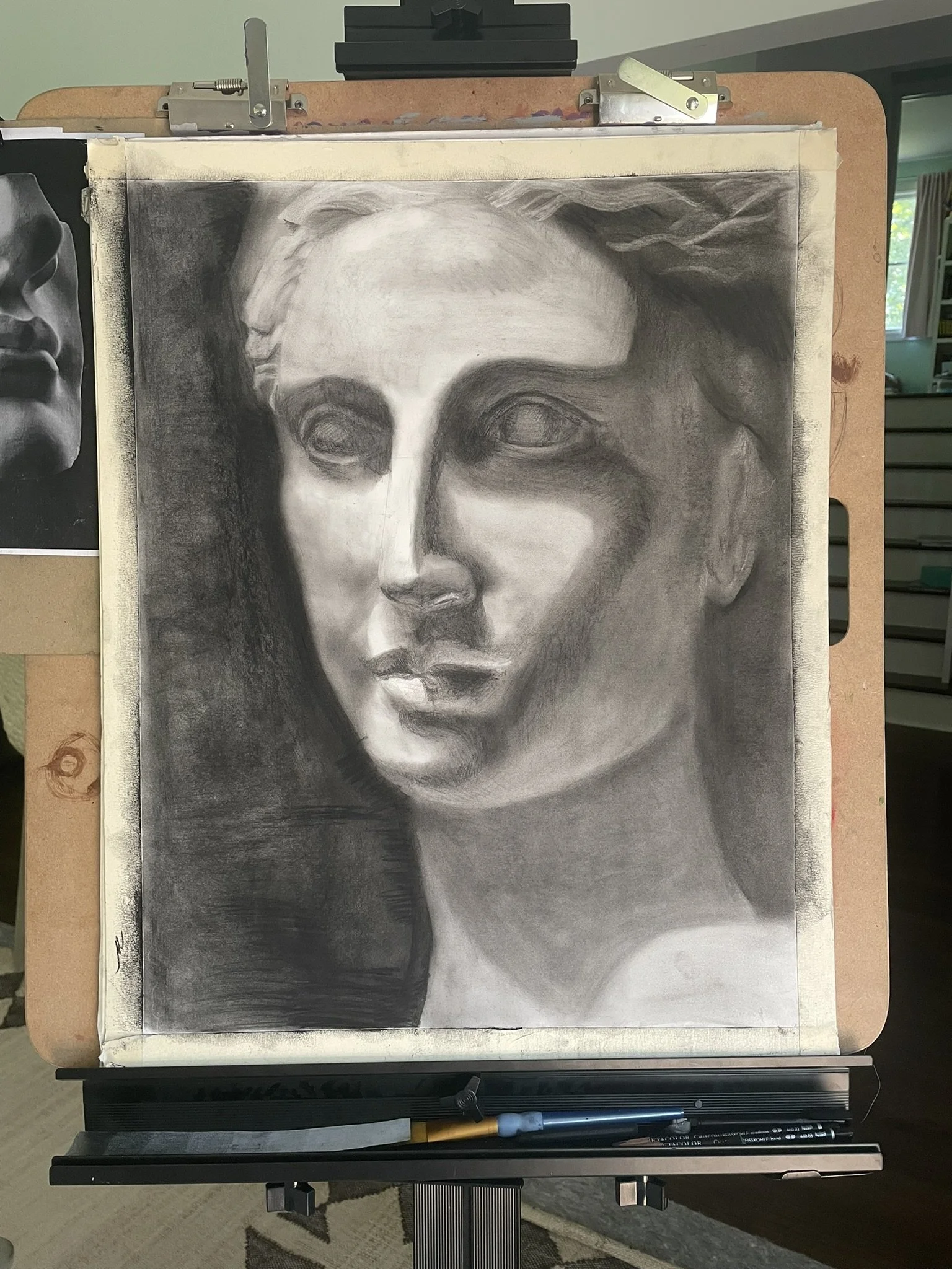Charcoal drawing of a woman's face on an easel, with soft shading and detailed features.