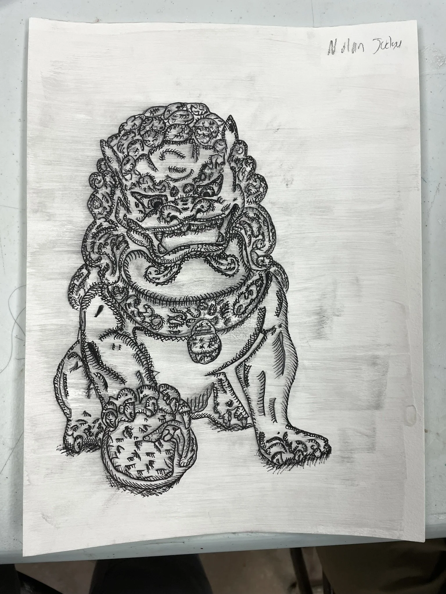 Black and white sketch of a Foo Dog statue with a ball in front of it, on a white piece of paper. Handwritten text 'Nolan Jackson' in the top right corner.
