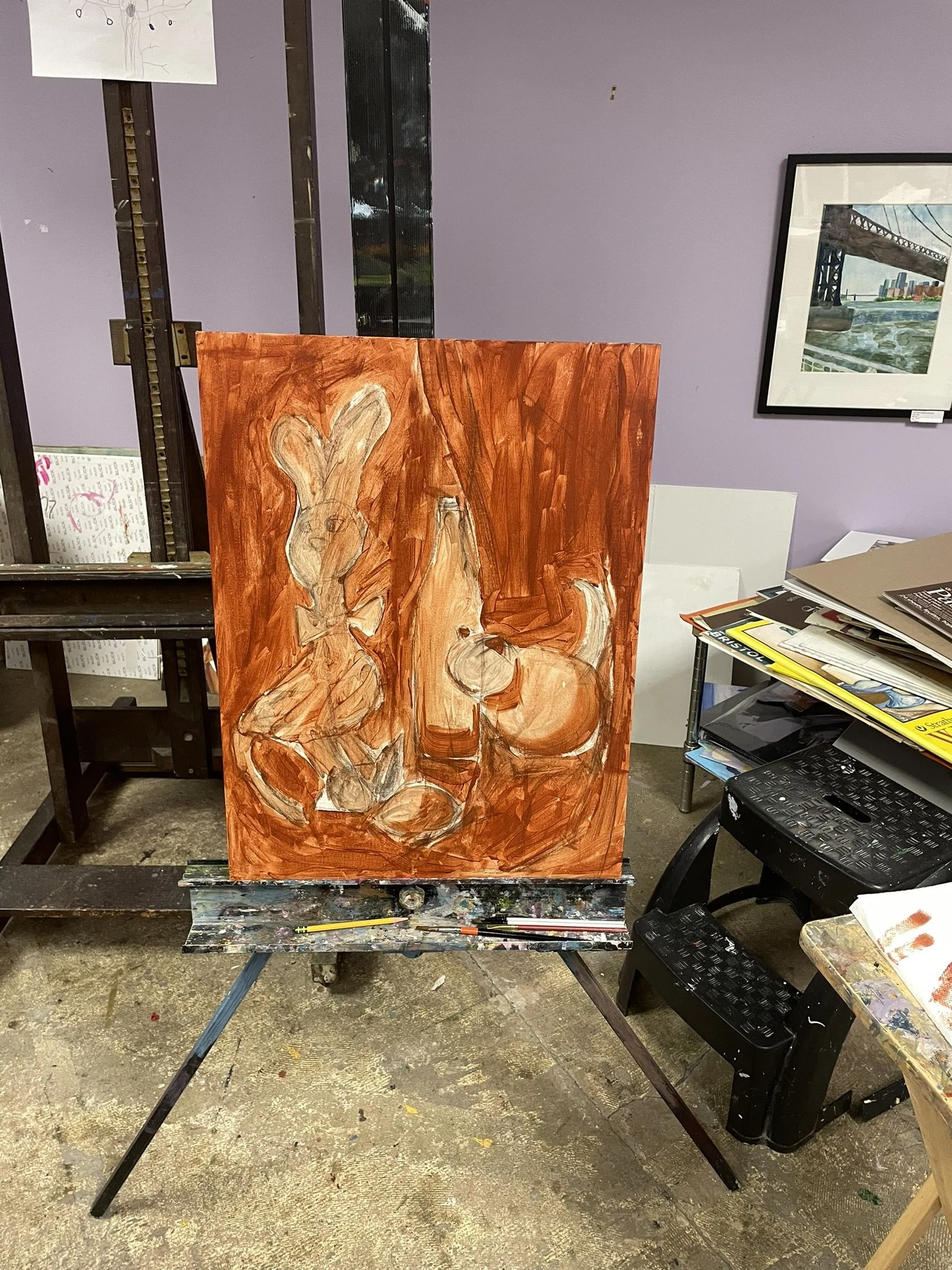 An abstract painting of a rabbit and a dog on a canvas, set up on an easel in an art studio with shelves, scattered art supplies, and artwork on the walls.