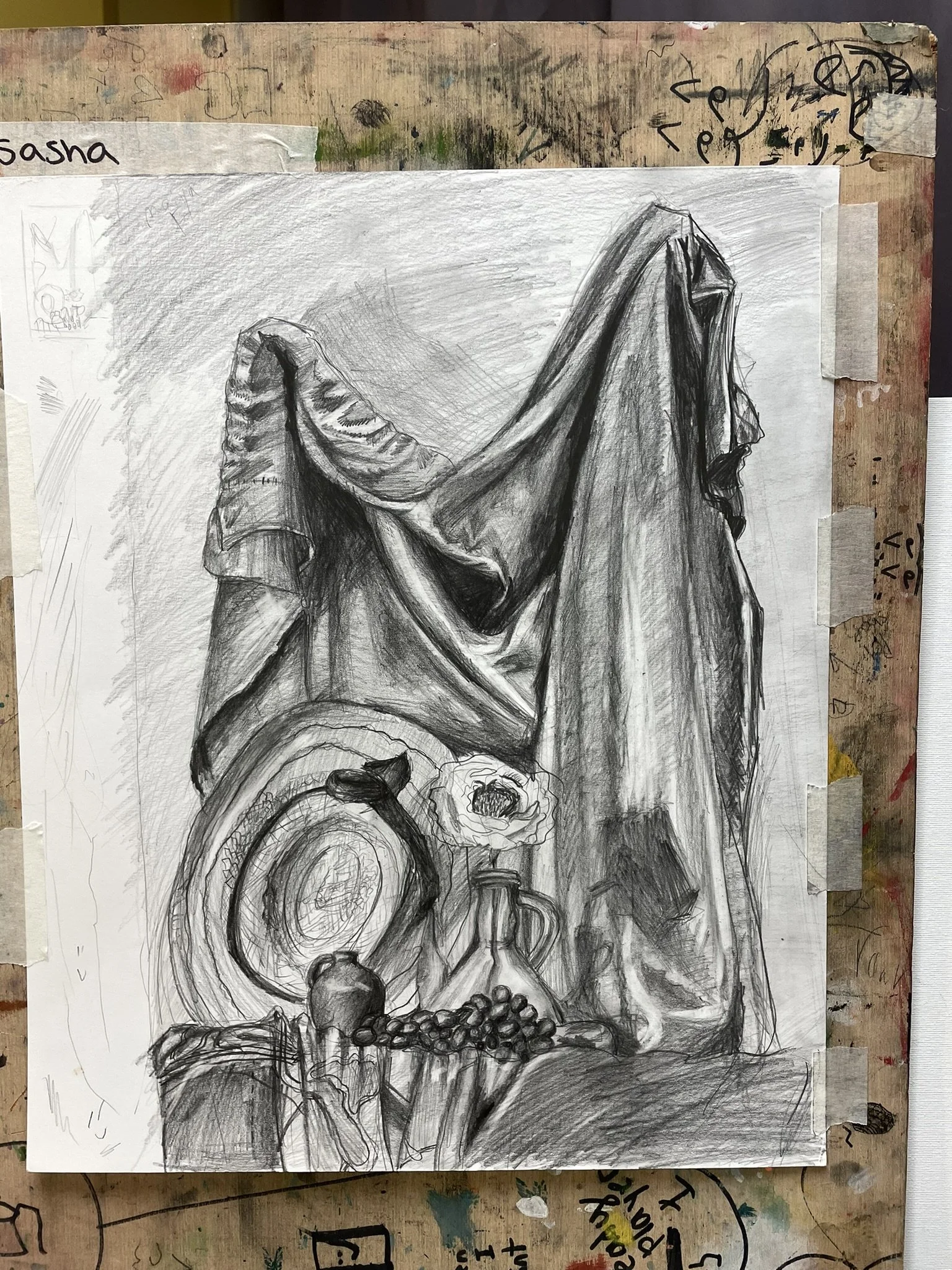 A detailed graphite drawing of a still life featuring a draped fabric, a plate, a hat, a flower in a vase, grapes, and miscellaneous objects on a table.