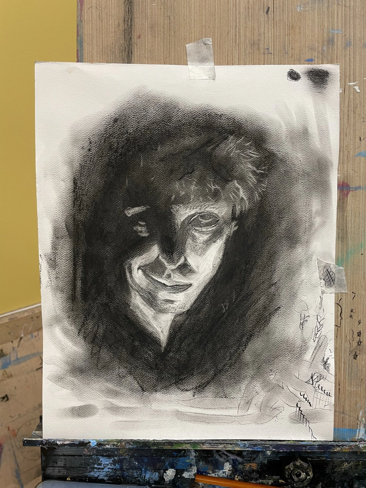 Black and white charcoal or pencil sketch of a smiling woman with curly hair, gazing slightly to the side, on a textured artist's paper.