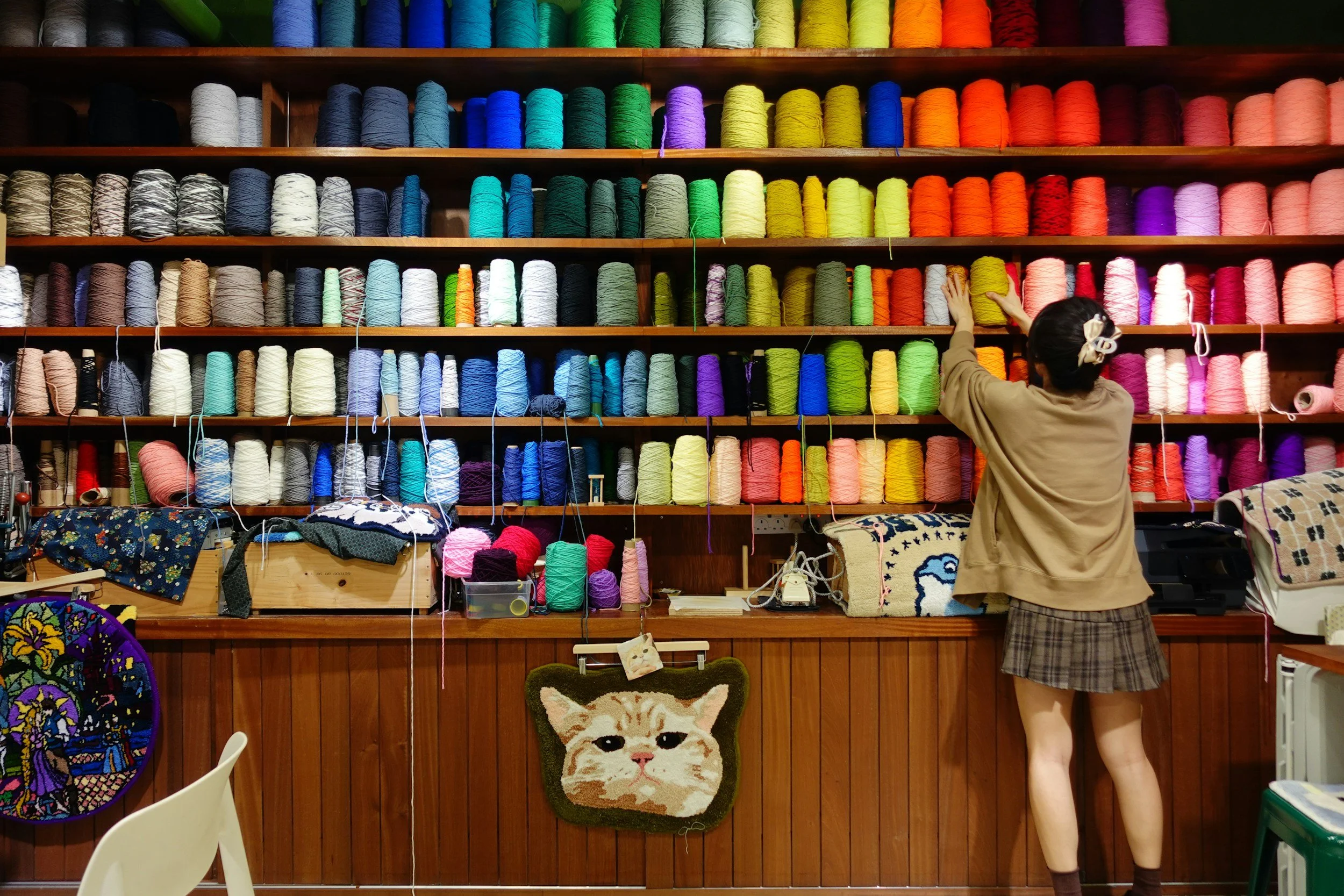 A woman arranging colorful yarn on wooden shelves in a craft store.
