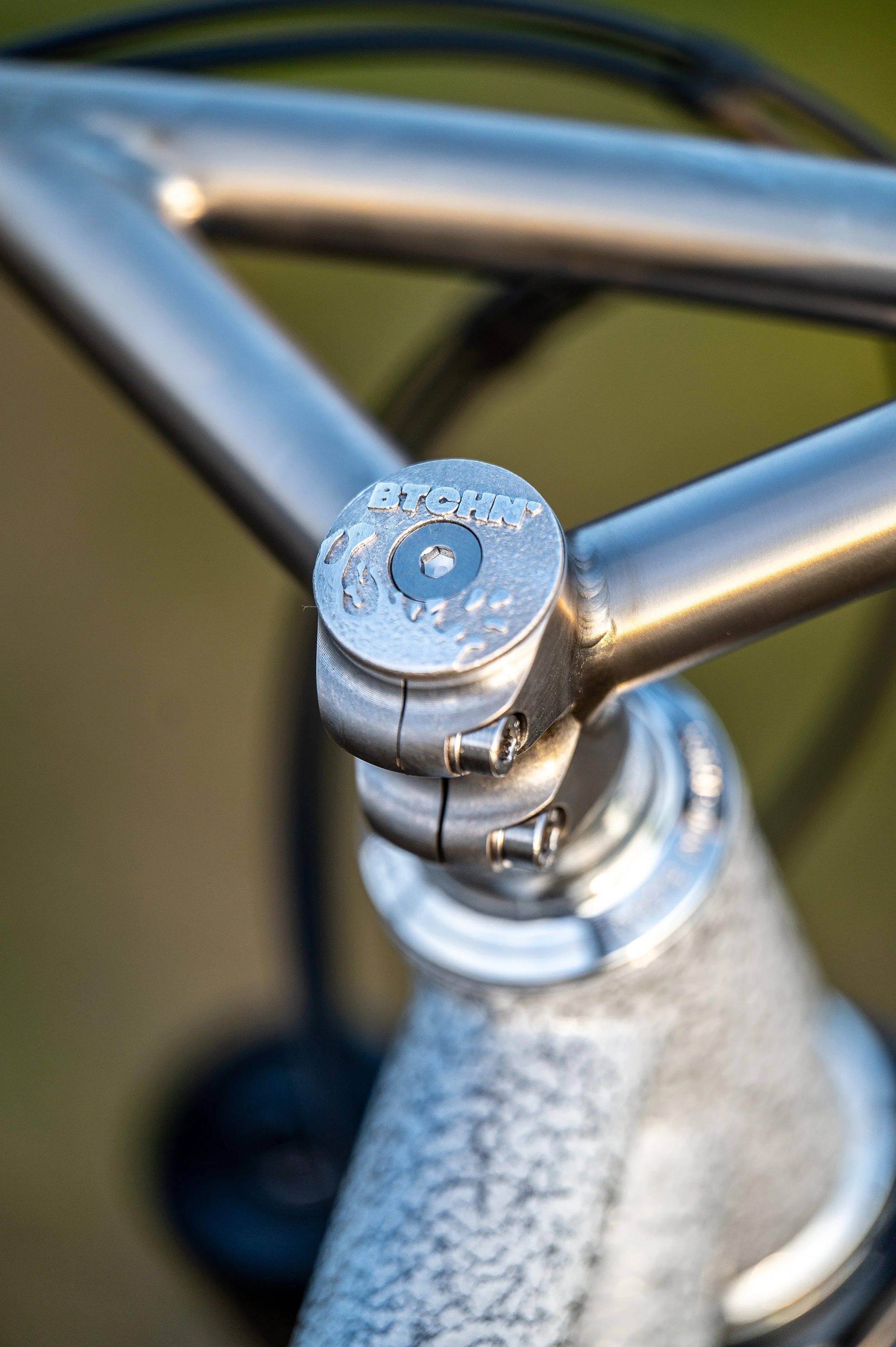 Close-up of a bicycle stem and handlebars, silver metal, branded 'Brompton'.