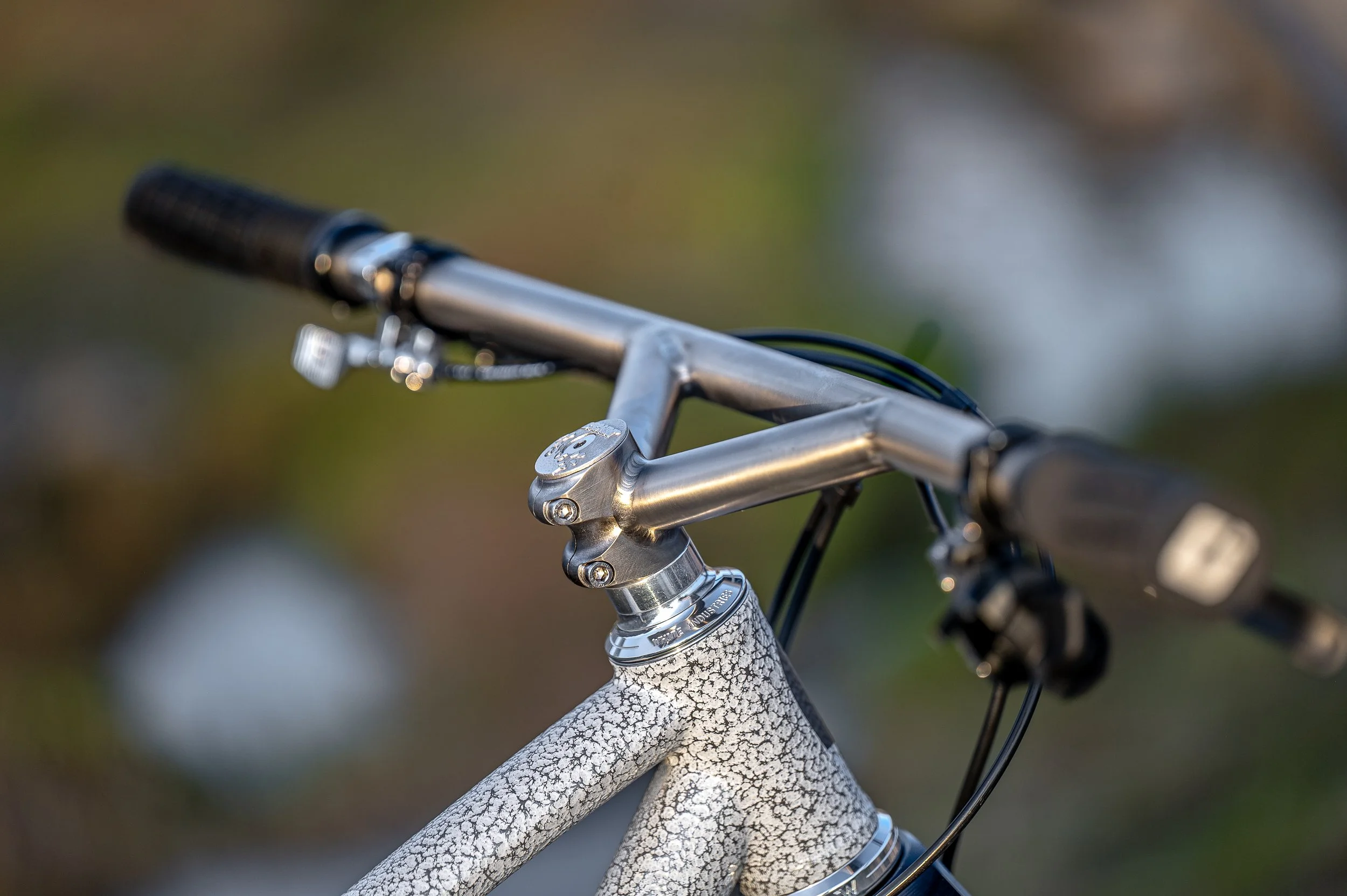 Close-up of a bicycle handlebar and top tube with textured gray paint, with blurred background.