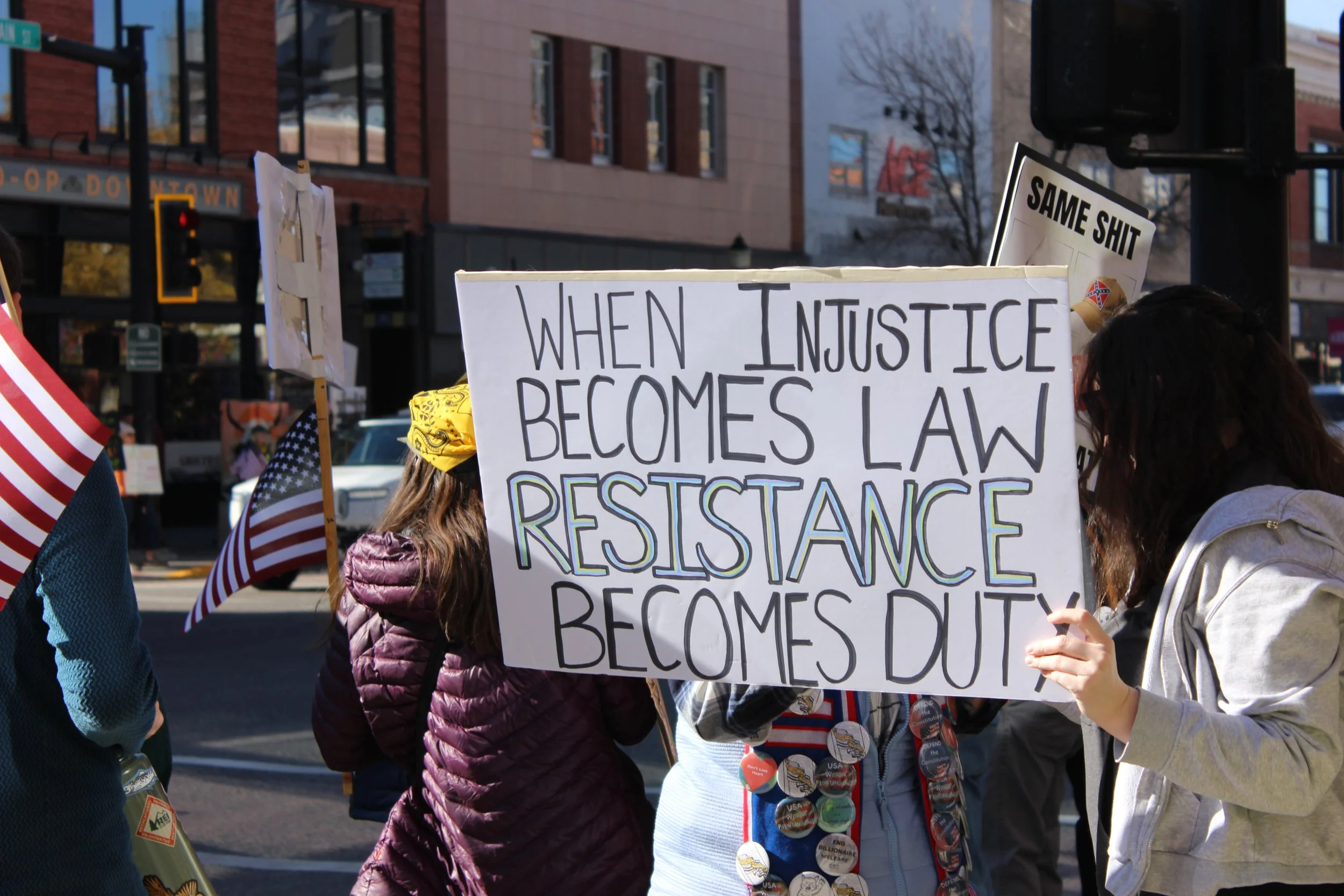 Protesters holding signs, including one that reads, 'When injustice becomes law resistance becomes duty,' in an urban street setting.