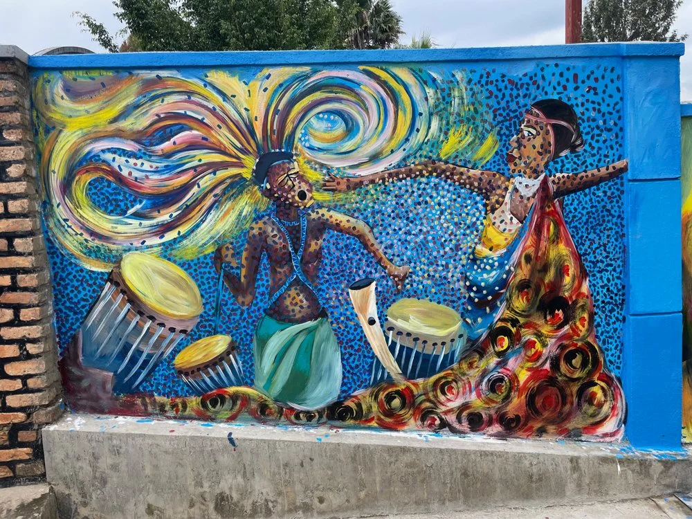 Mural of two women dancing with drums, vibrant colors, swirling patterns, and a blue background.