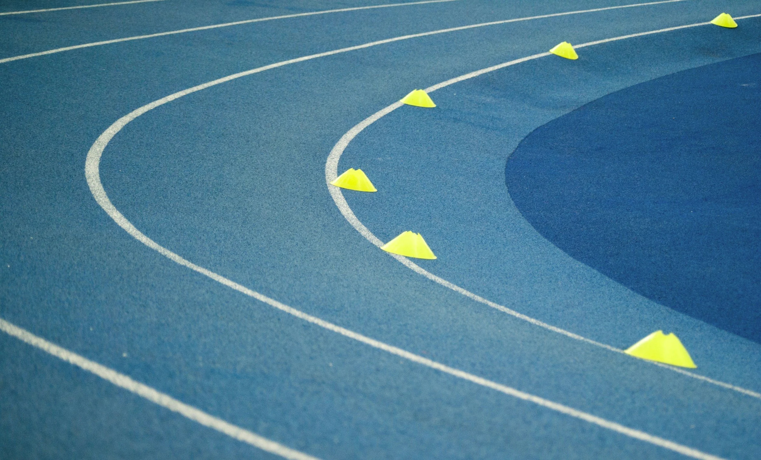 A blue running track with white lane markings and yellow cones.