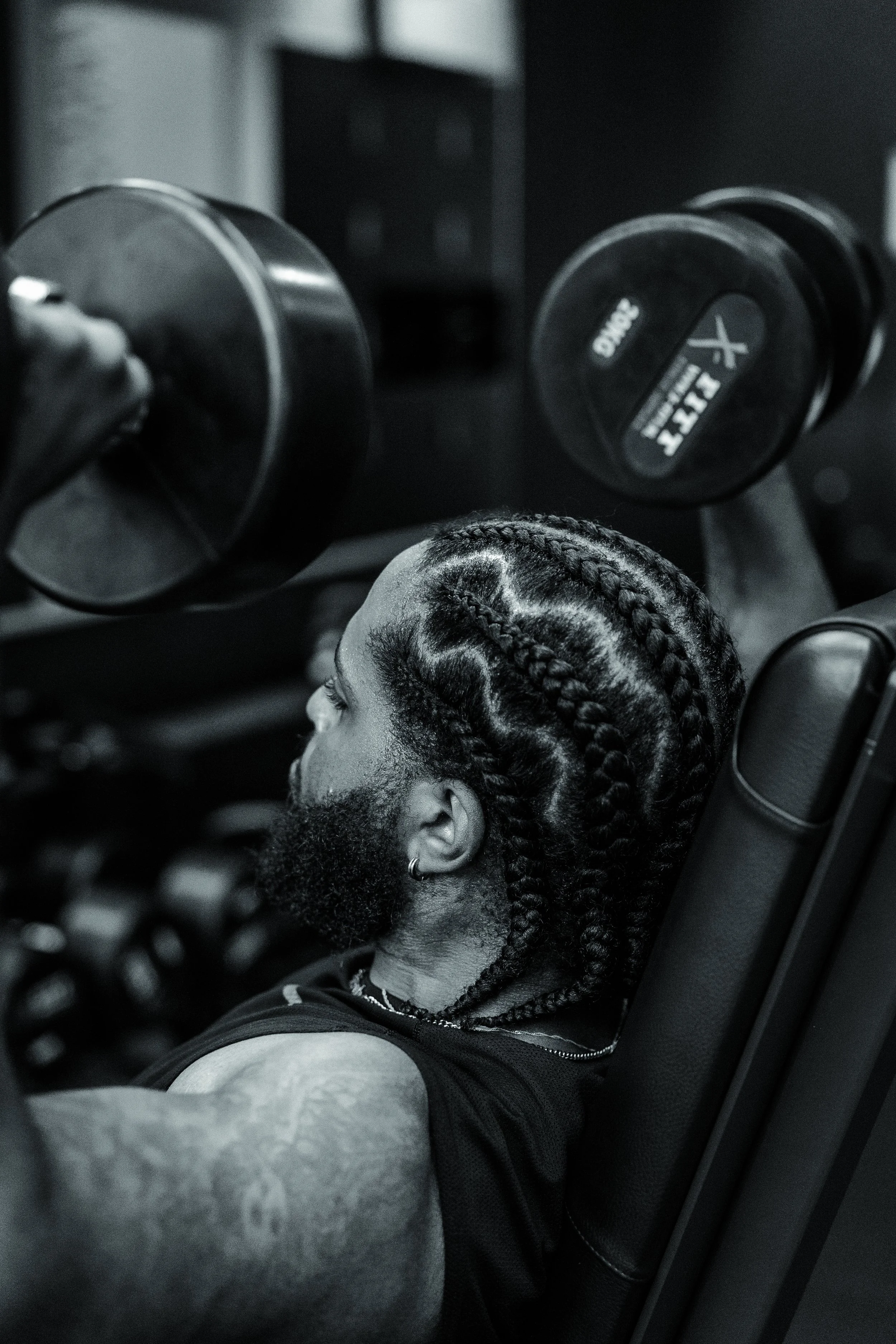 A person with braids and a beard lifting dumbbells in a gym.