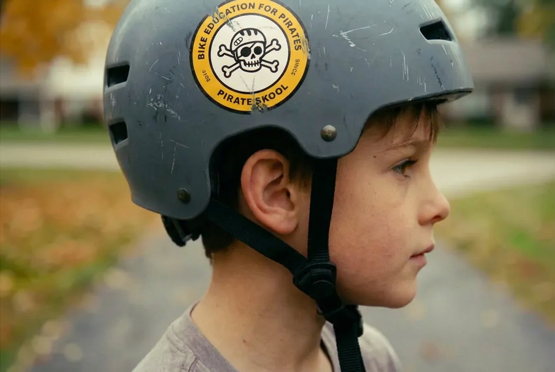 Profile of a young boy wearing a gray helmet with a sticker that says 'Bike Education for Pirates' and features a skull with a helmet and crossbones.