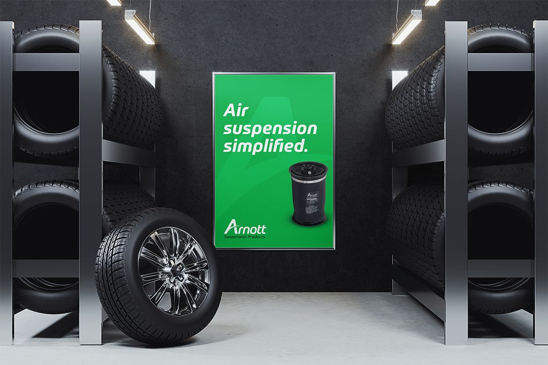 A display of tires on metal racks in a store or warehouse with a green poster advertising Arnott suspension products in the background.