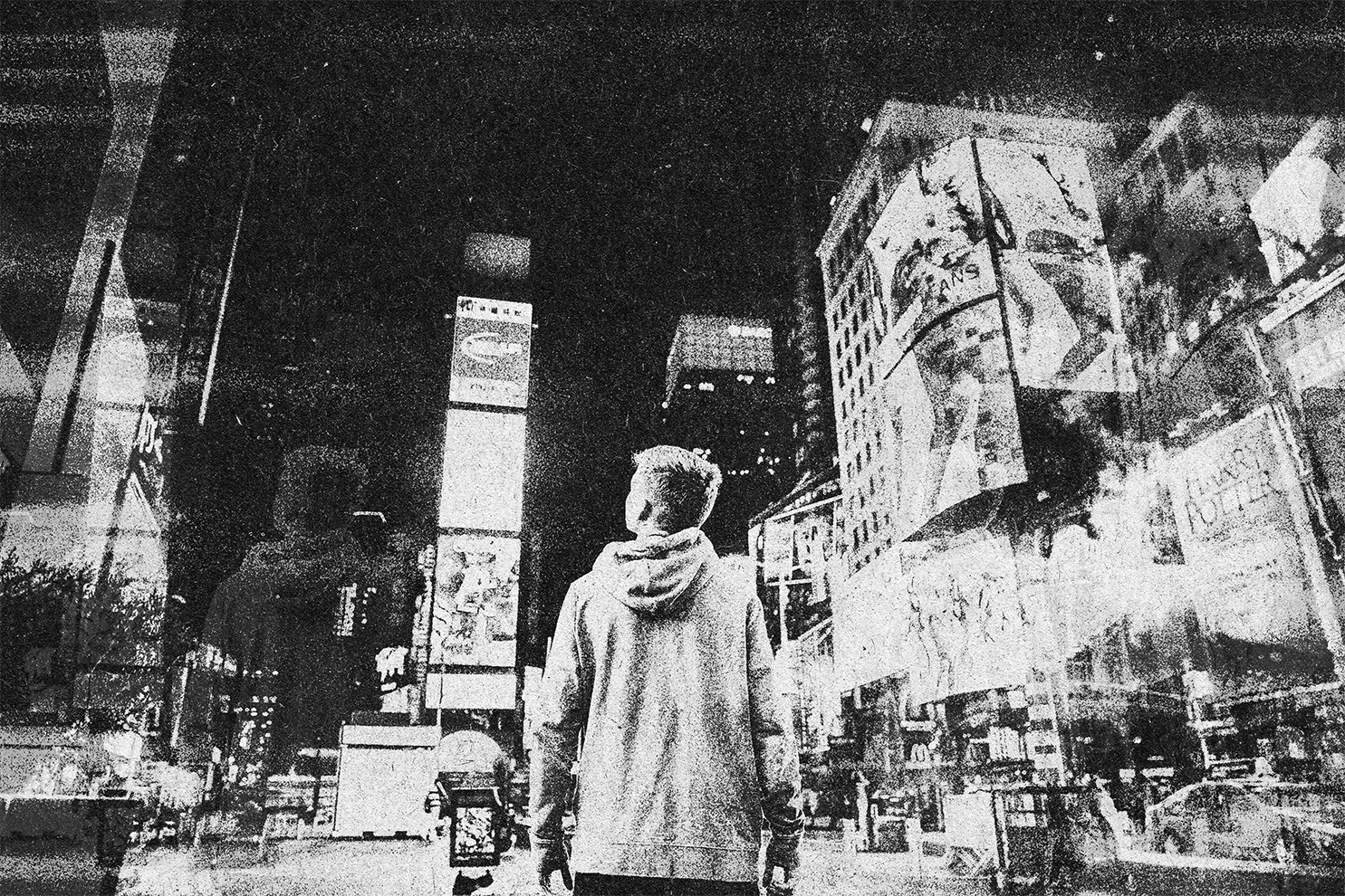 A person with short hair wearing a hoodie, viewed from the back, walking in a busy urban city at night with bright digital billboards and signs illuminated around.