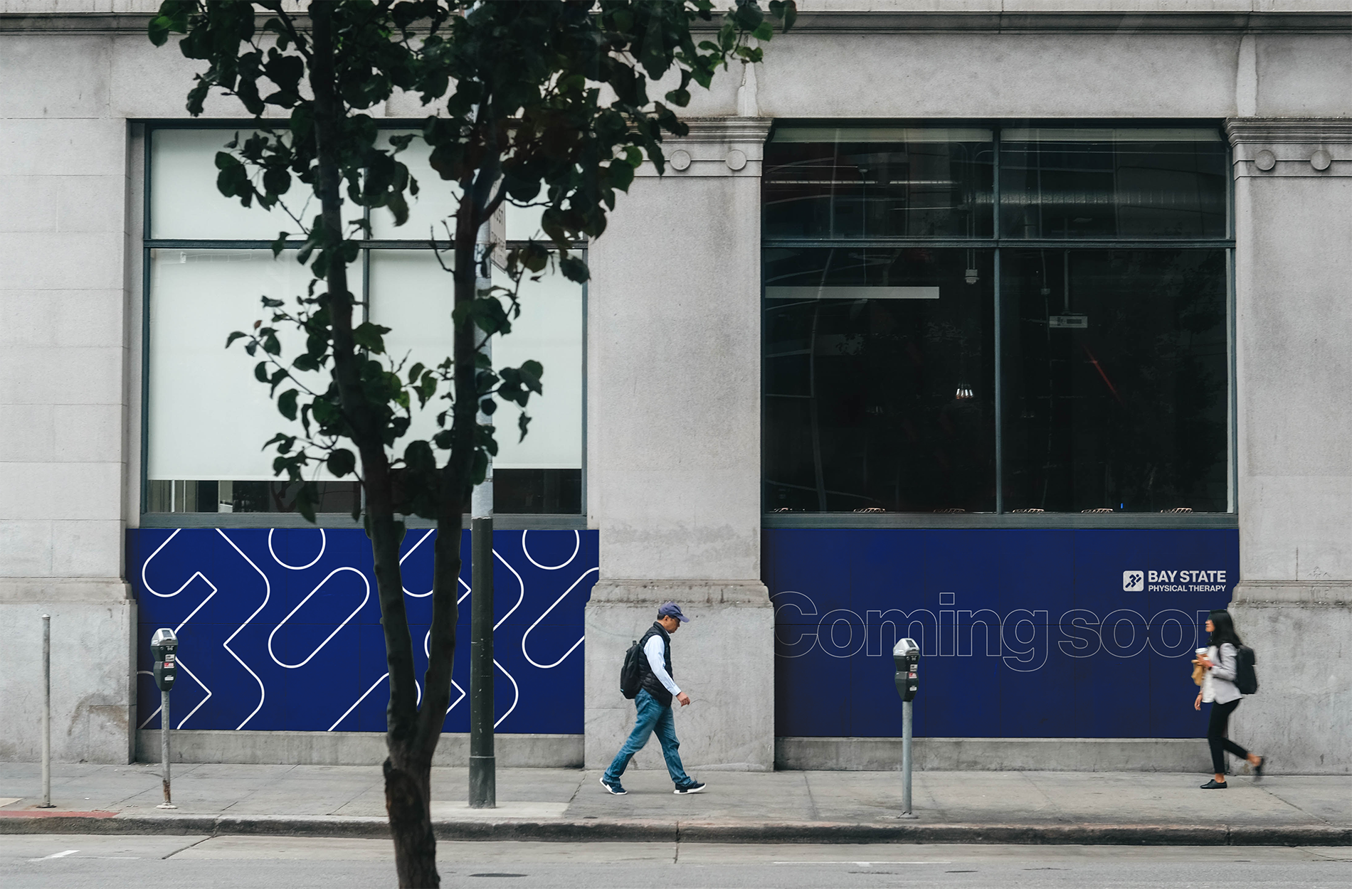 City street scene with two pedestrians walking past a building with a sign that reads 'coming soon' and 'Bay State Physical Therapy'