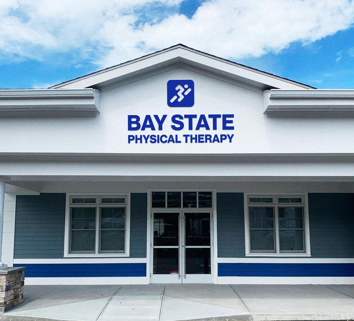 Front of a building with a sign that reads 'Bay State Physical Therapy' and a logo with a running shoe above the sign.