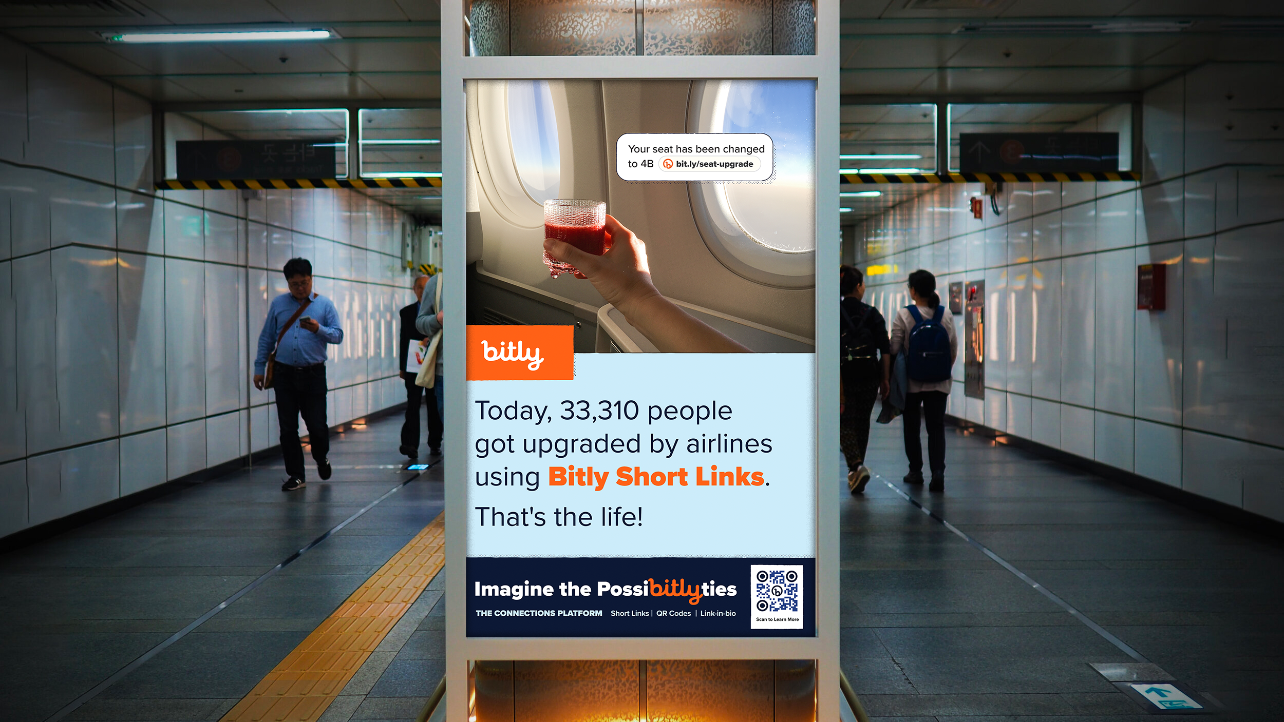 Digital advertisement in a subway station featuring a hand holding a glass of red juice and a notification about seat upgrade. The ad mentions that 33,310 people today have upgraded their seats using Bitly Short Links, with the slogan "Imagine the Possibilities" and a QR code for more information.