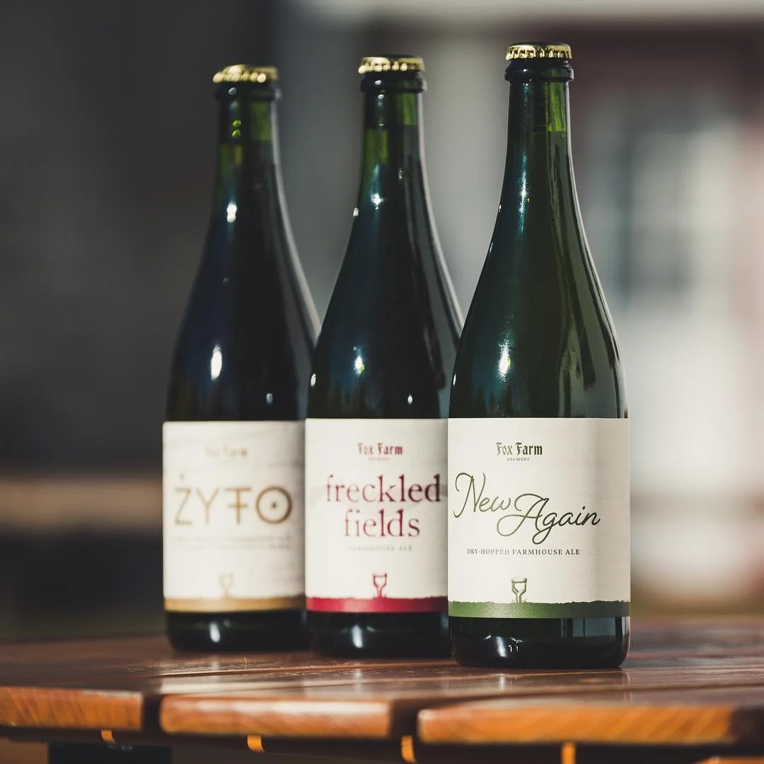 Three dark glass beer bottles with labels on a wooden surface, with a blurred background.