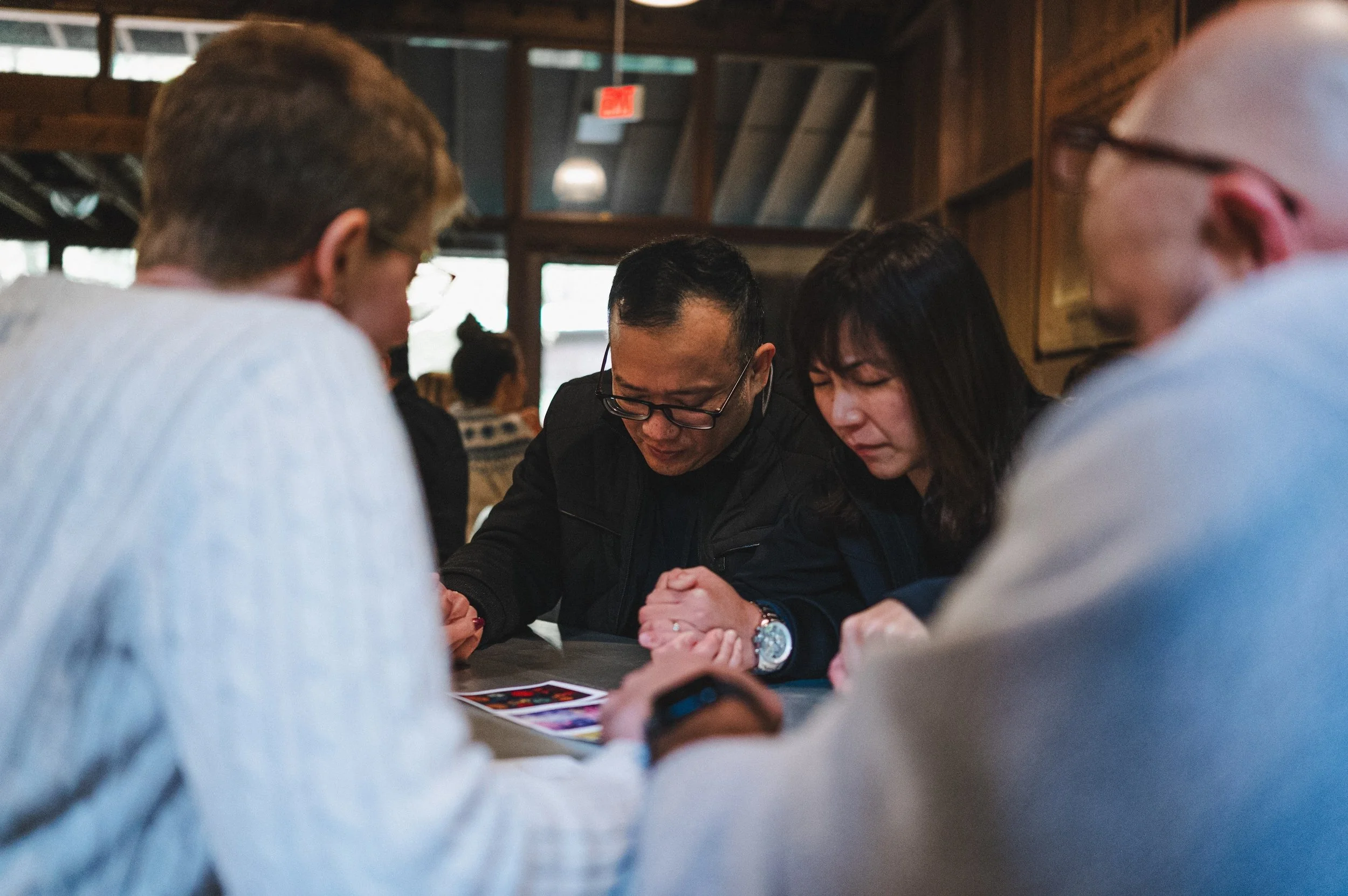 Four people sitting at a table in a restaurant, looking at a phone or tablet together.