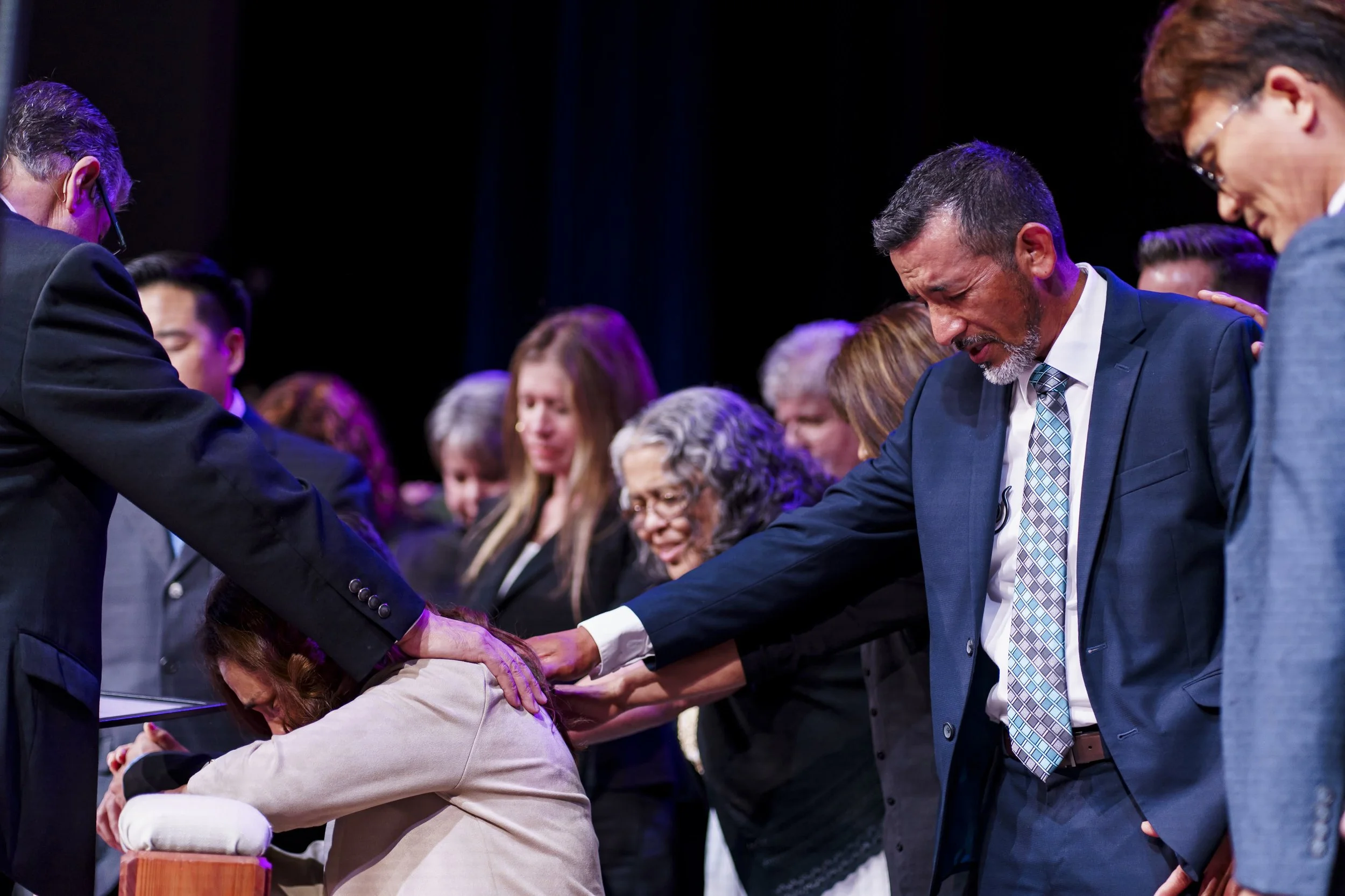 People praying with their hands on a woman's head at a religious gathering.