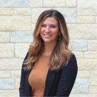 A woman with long hair smiling against a stone wall background.