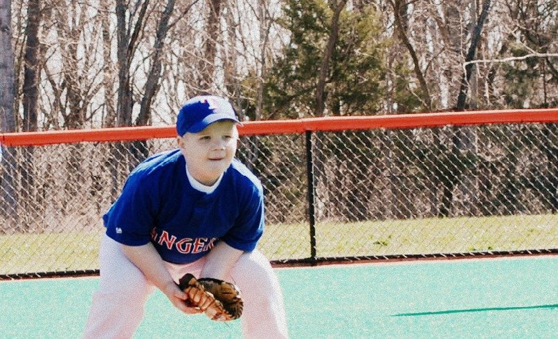 Young boy wearing a blue baseball jersey, white pants, and a blue cap, crouching on a baseball field with a glove in his hands.