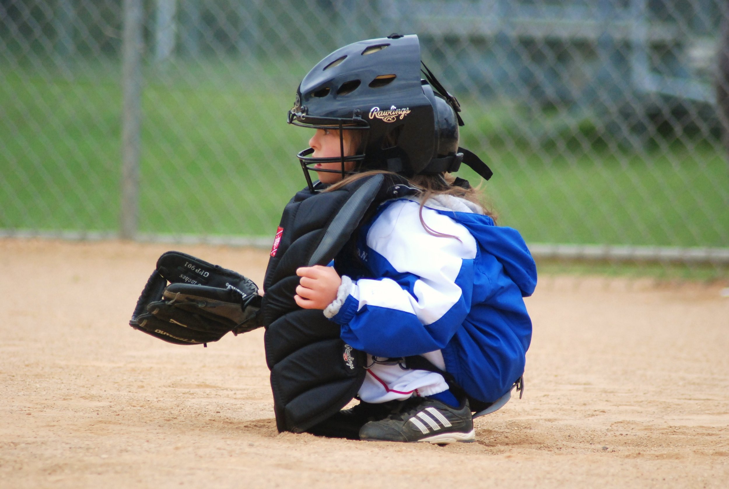A young baseball catcher crouching on the field in full gear, including a helmet and padded clothing.