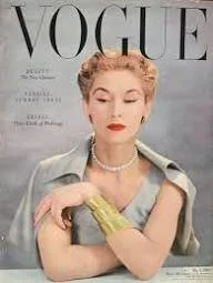 Vintage Vogue magazine cover featuring a woman with short blonde hair, red lipstick, pearl necklace, and a greenish-gray outfit, holding a yellow flower.