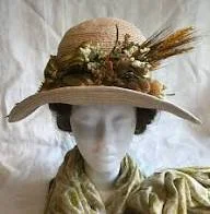 A mannequin wearing a wide-brimmed straw hat decorated with flowers, wheat, and greenery, and dressed in a vintage-style outfit.