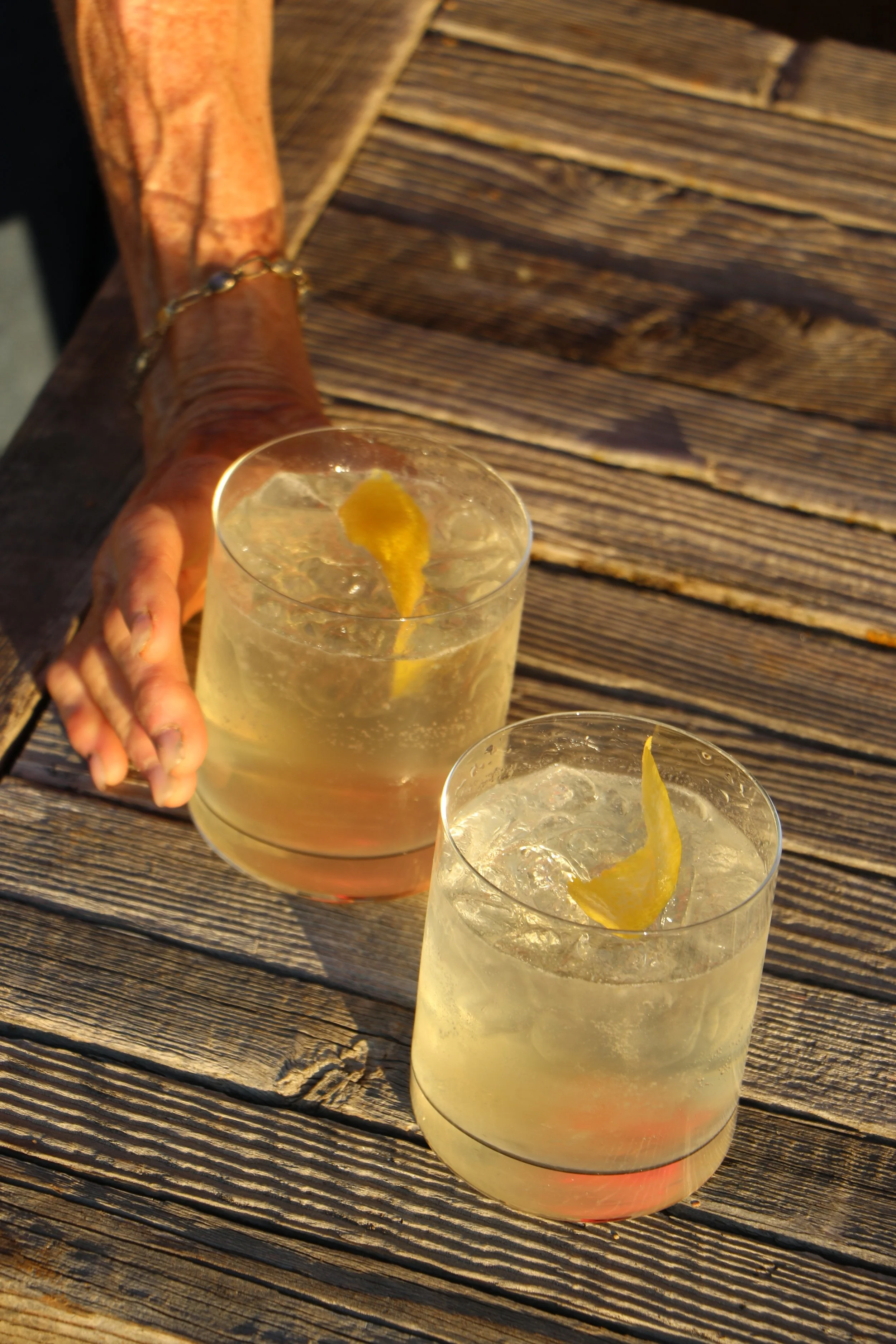 Two glasses of lemonade with lemon slices on a wooden table outdoors.