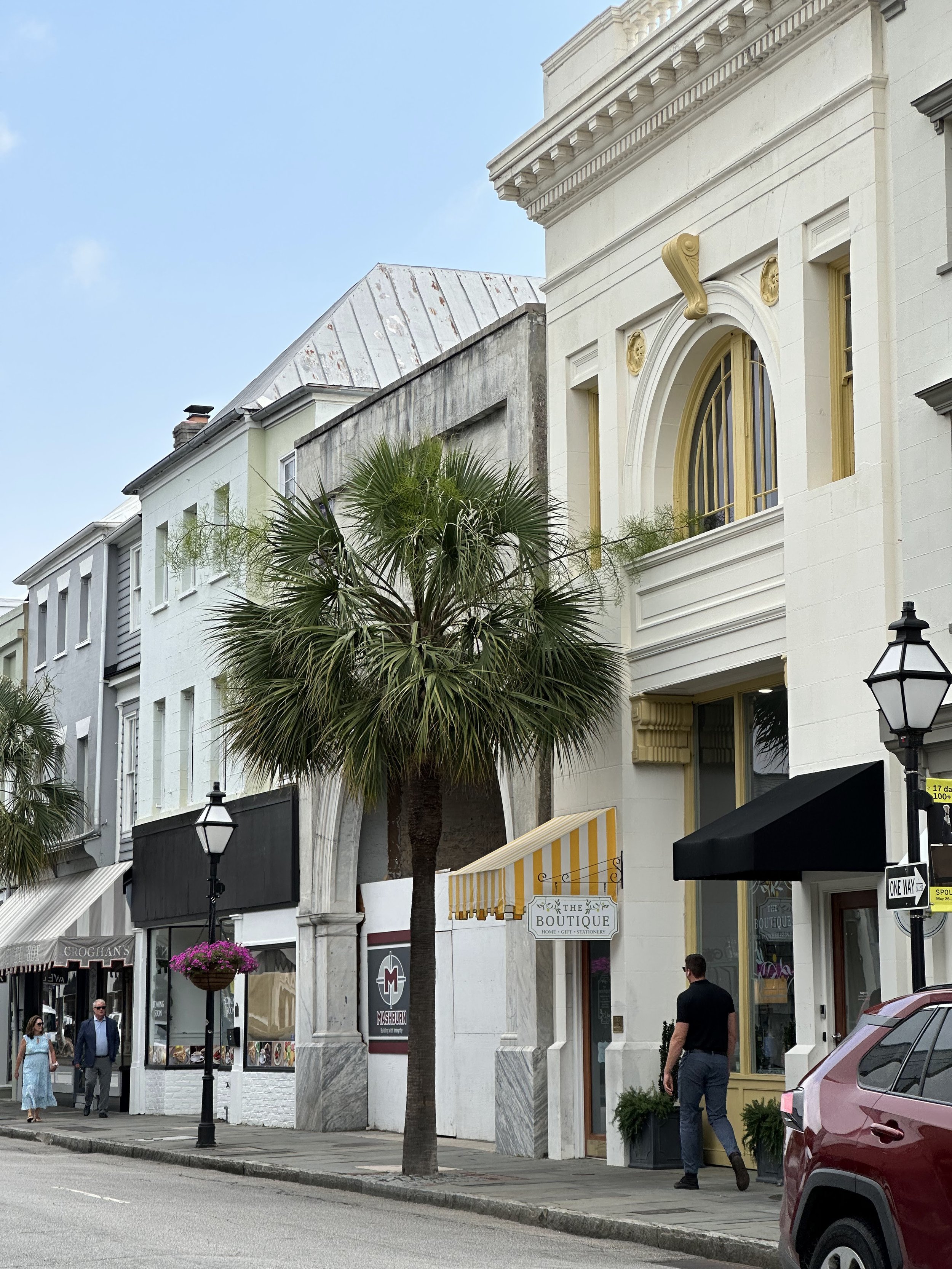 Street view with palm trees, historic buildings, storefronts, and people walking on the sidewalk.