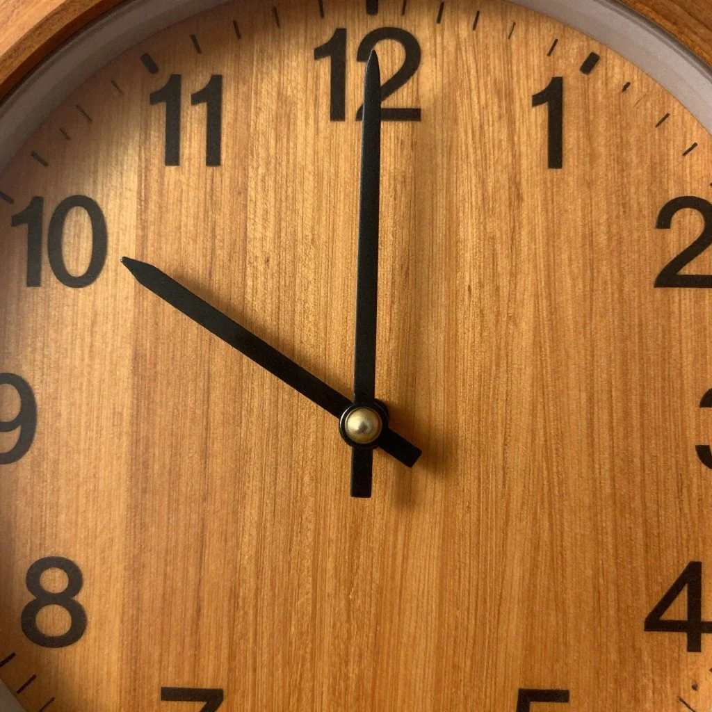 A round wooden wall clock showing 10:00 with black hour and minute hands and black numbers on a light wood background.