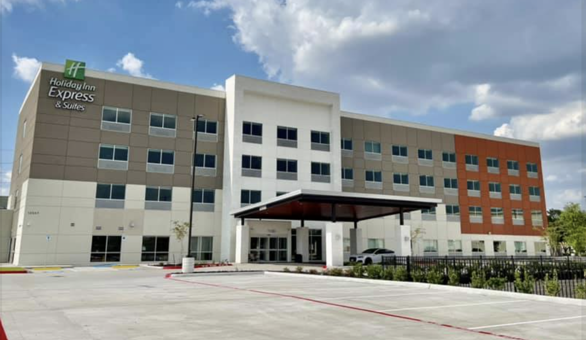 Exterior of a Holiday Inn Express & Suites hotel with a parking lot in front, partly cloudy sky.