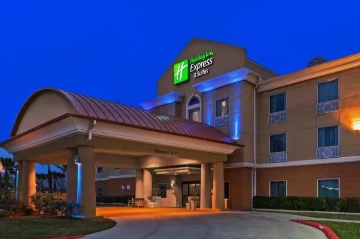 Exterior of a Holiday Inn Express & Suites hotel during evening with illuminated signs and lit entrance.