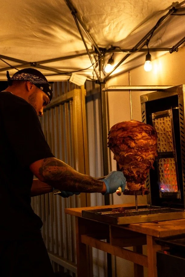 Hombre preparando carne en un espetón en un puesto de comida callejera en la noche.