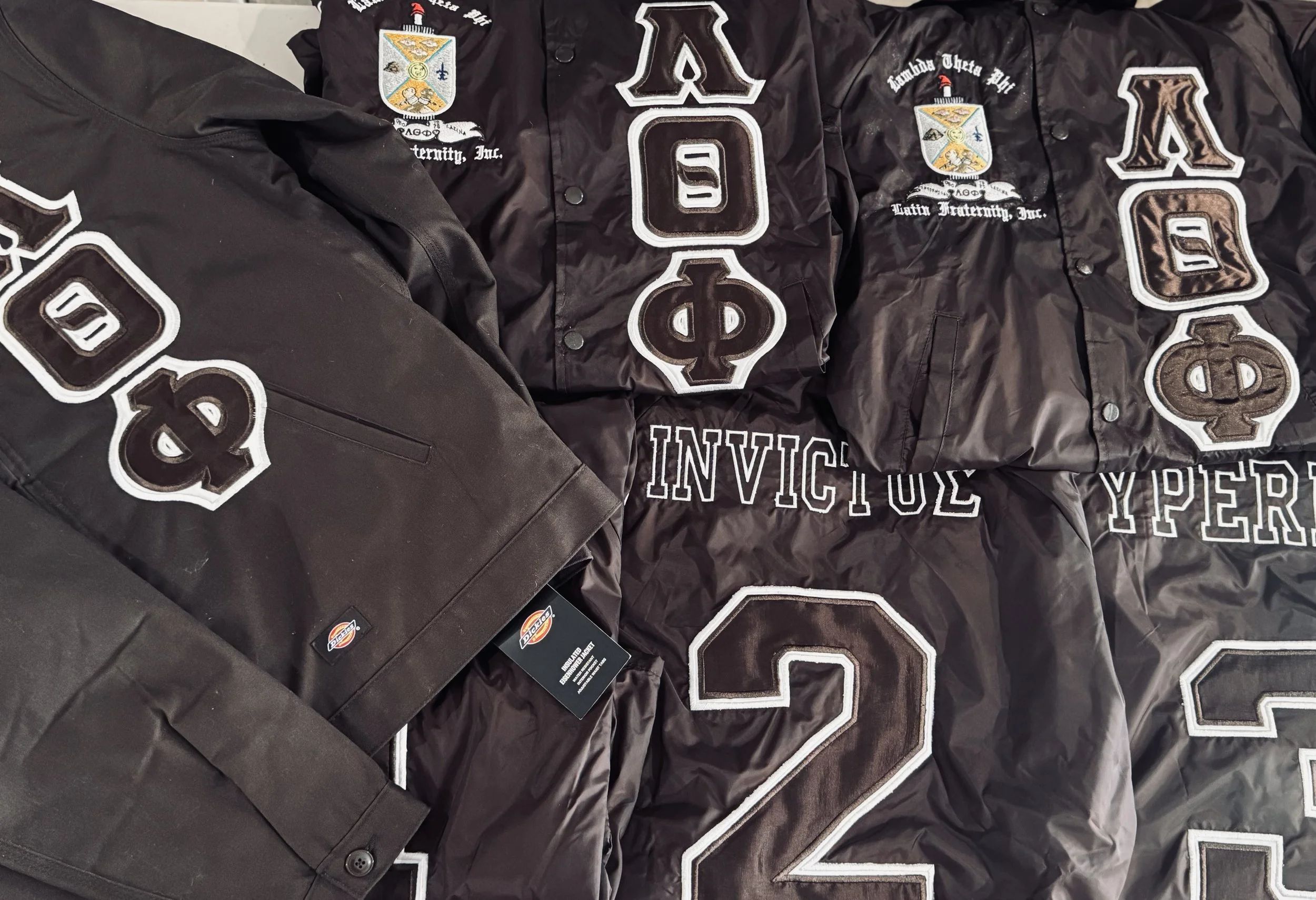 Black jackets with patches and embroidery featuring seals, Greek letters, and words such as "Invictus" and "Hyper."