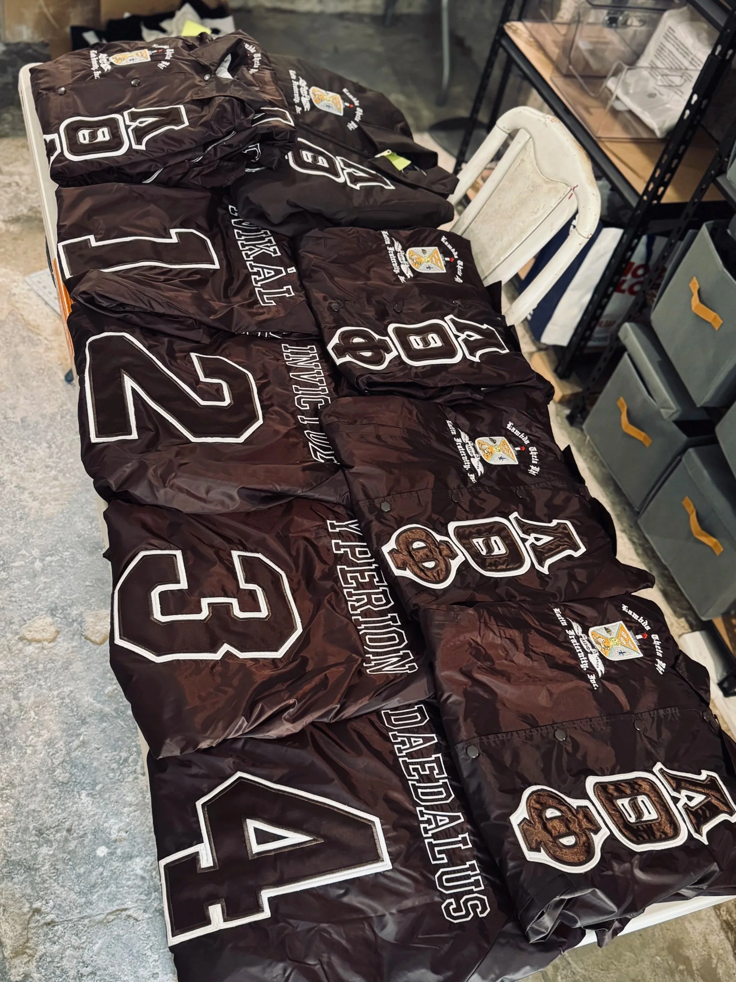 A table covered with black jackets bearing the logos and name of the 2023 Dalesday USA event, including large numbers 1, 2, 3, and 4, along with a teddy bear graphic and the text "2023 Dalesday USA".