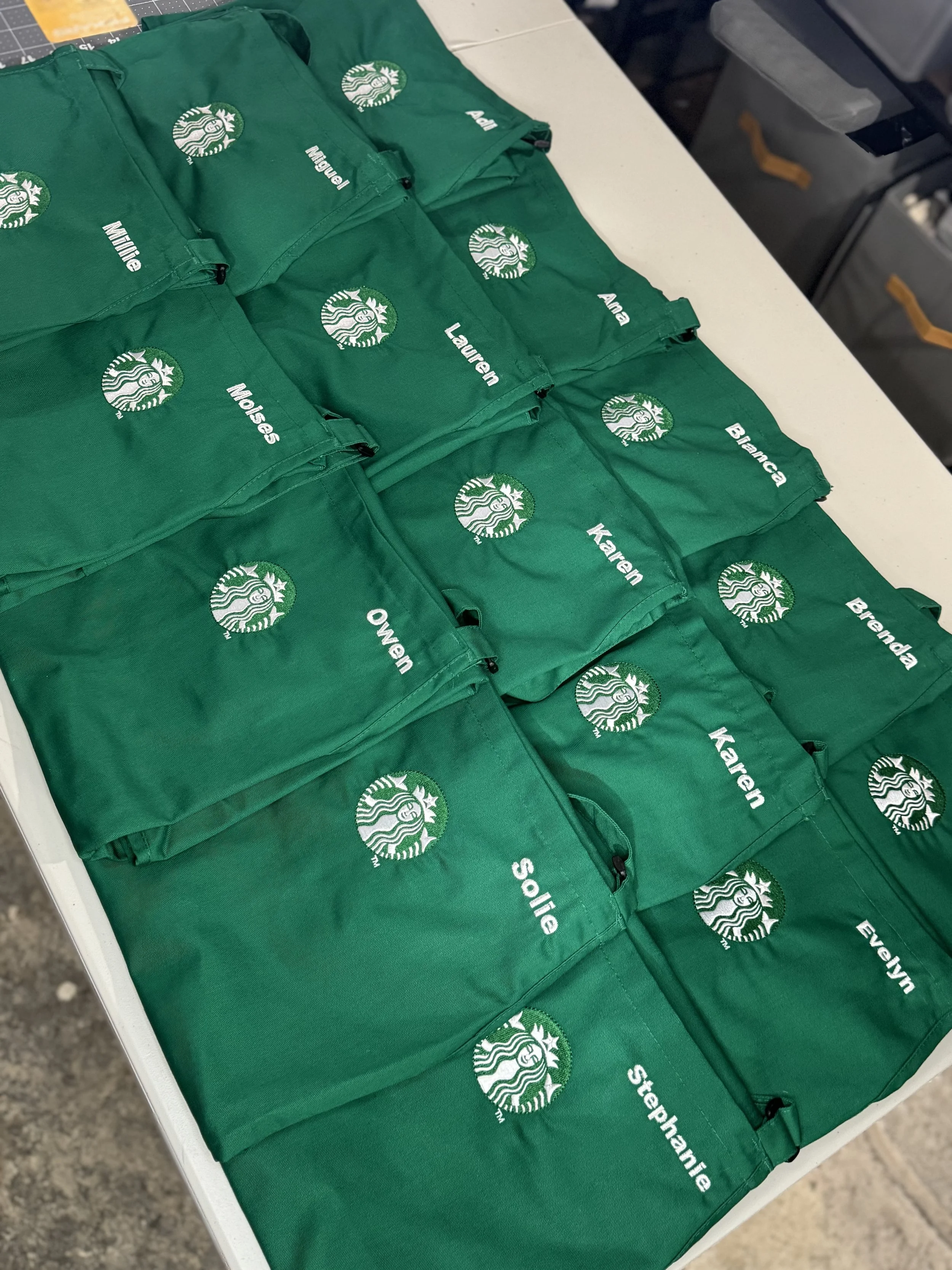Green Starbucks apron pouches with individual name labels arranged on a table.