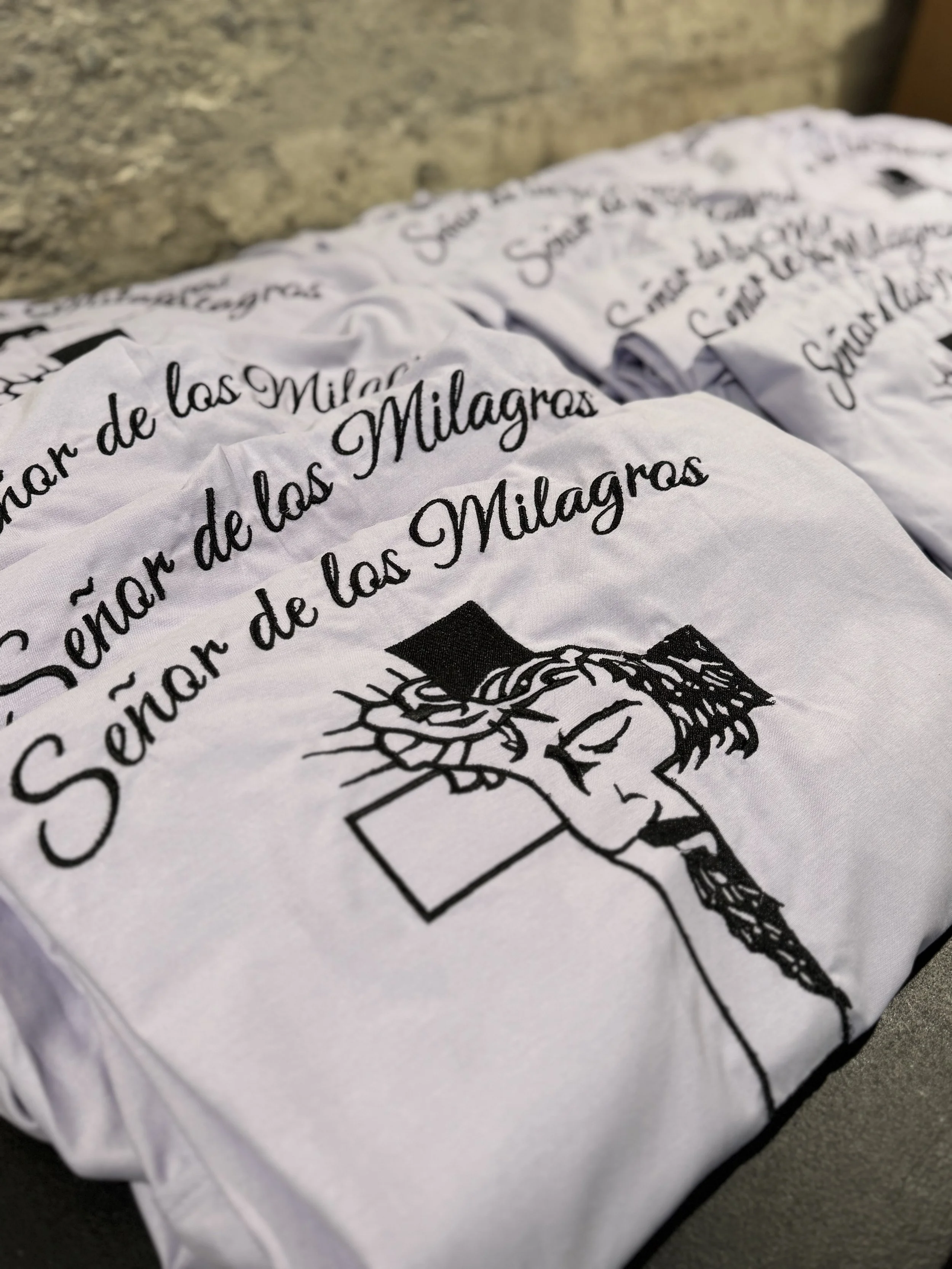 White t-shirt with black text and a drawing of Jesus Christ wearing a crown of thorns and a crown, with the phrase "Señor de las Milagros" printed on it.