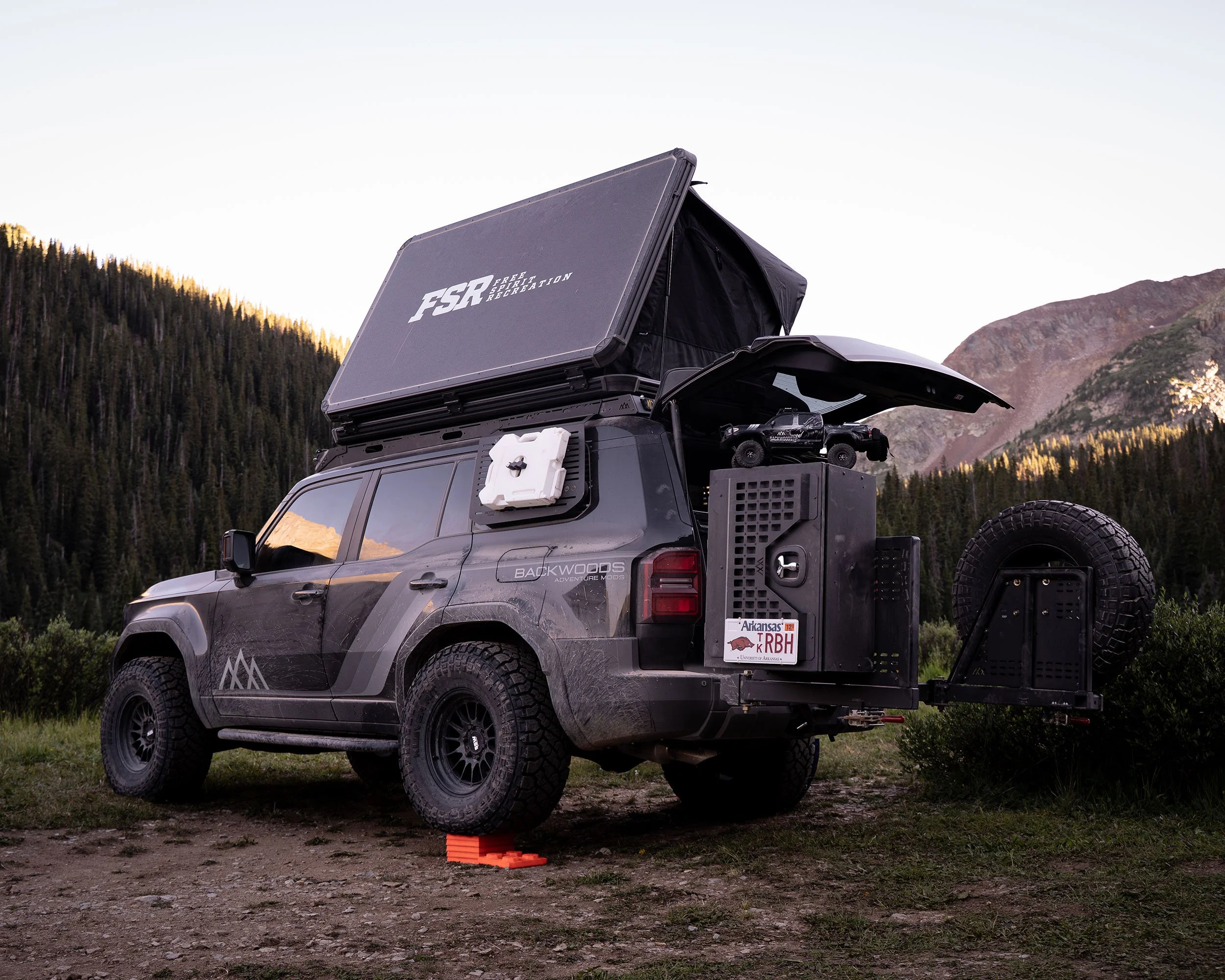 Off-road vehicle outfitted with camping gear and equipment, set in a mountainous outdoor landscape.